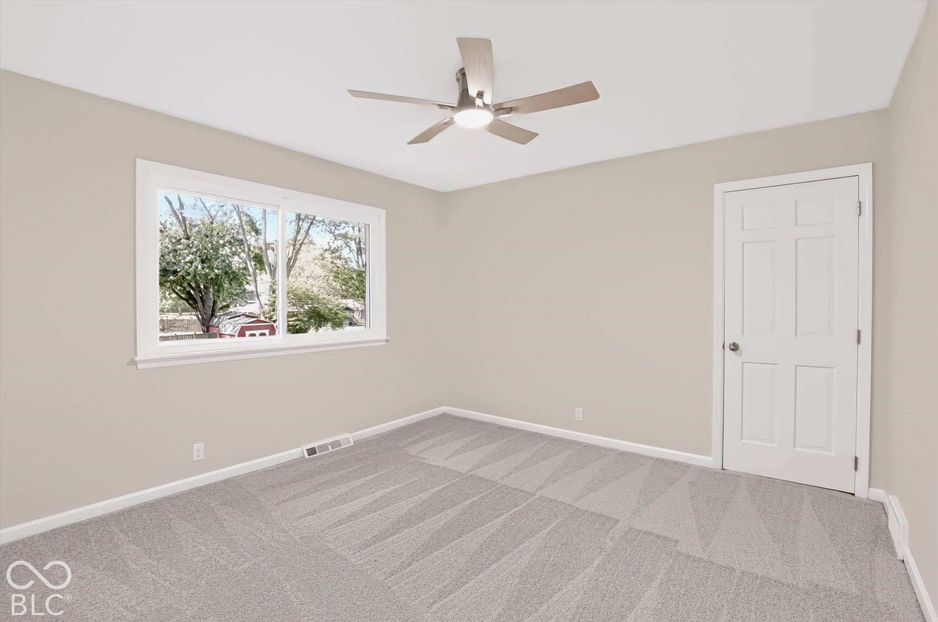 Neutral-toned interior featuring wall-to-wall carpeting, a multi-pane sliding window, and a ceiling fan with integrated lighting
