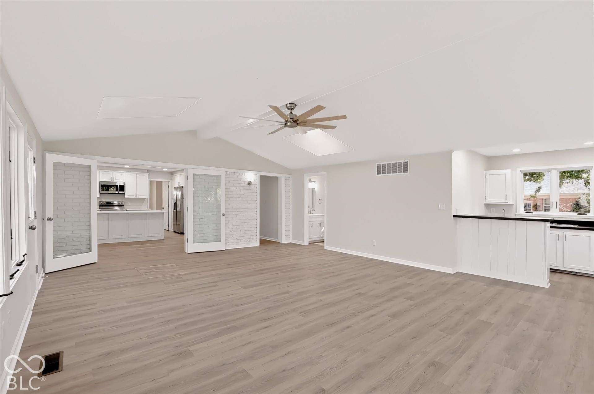 Open-concept interior featuring vaulted ceilings, wood-finish flooring, a skylight, and double French doors with frosted glass inserts