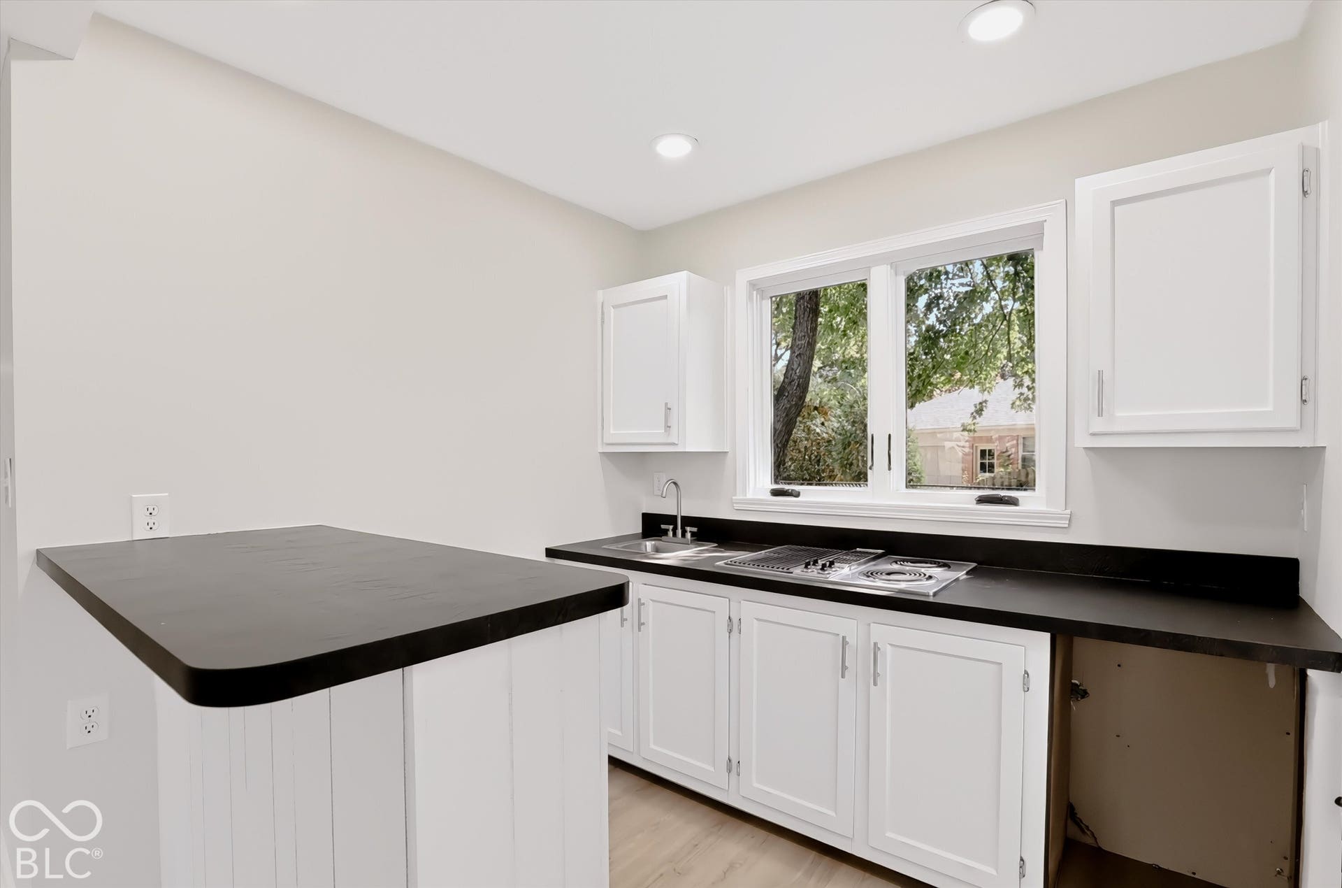 White cabinetry, dark solid-surface countertops, peninsula workspace, drop-in sink with gooseneck faucet, and wood-finish flooring