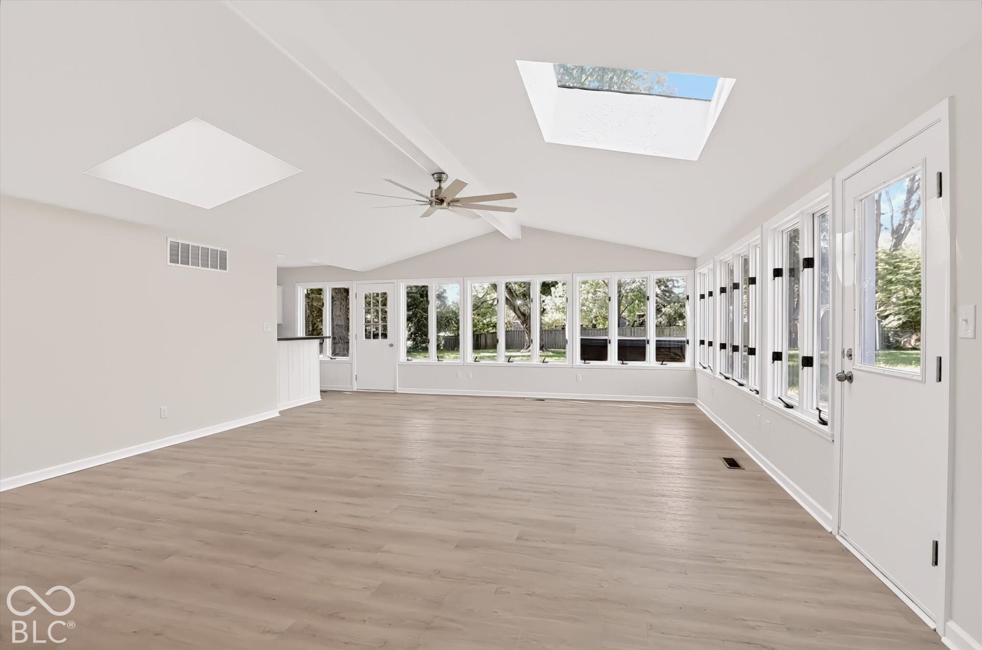 Vaulted ceiling sunroom featuring wood-finish flooring, two large skylights, expansive multi-pane windows, and a central ceiling fan