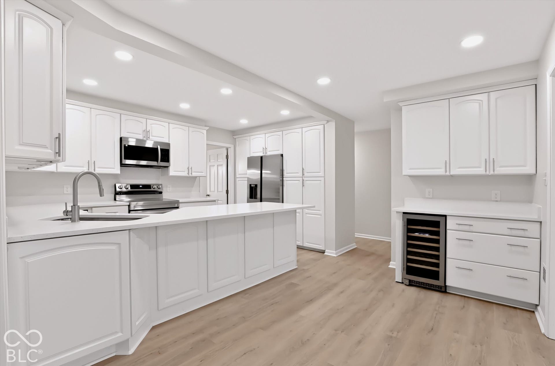 Kitchen featuring white cabinetry, solid-surface countertops, wood-finish flooring, recessed lighting, and a built-in wine cooler