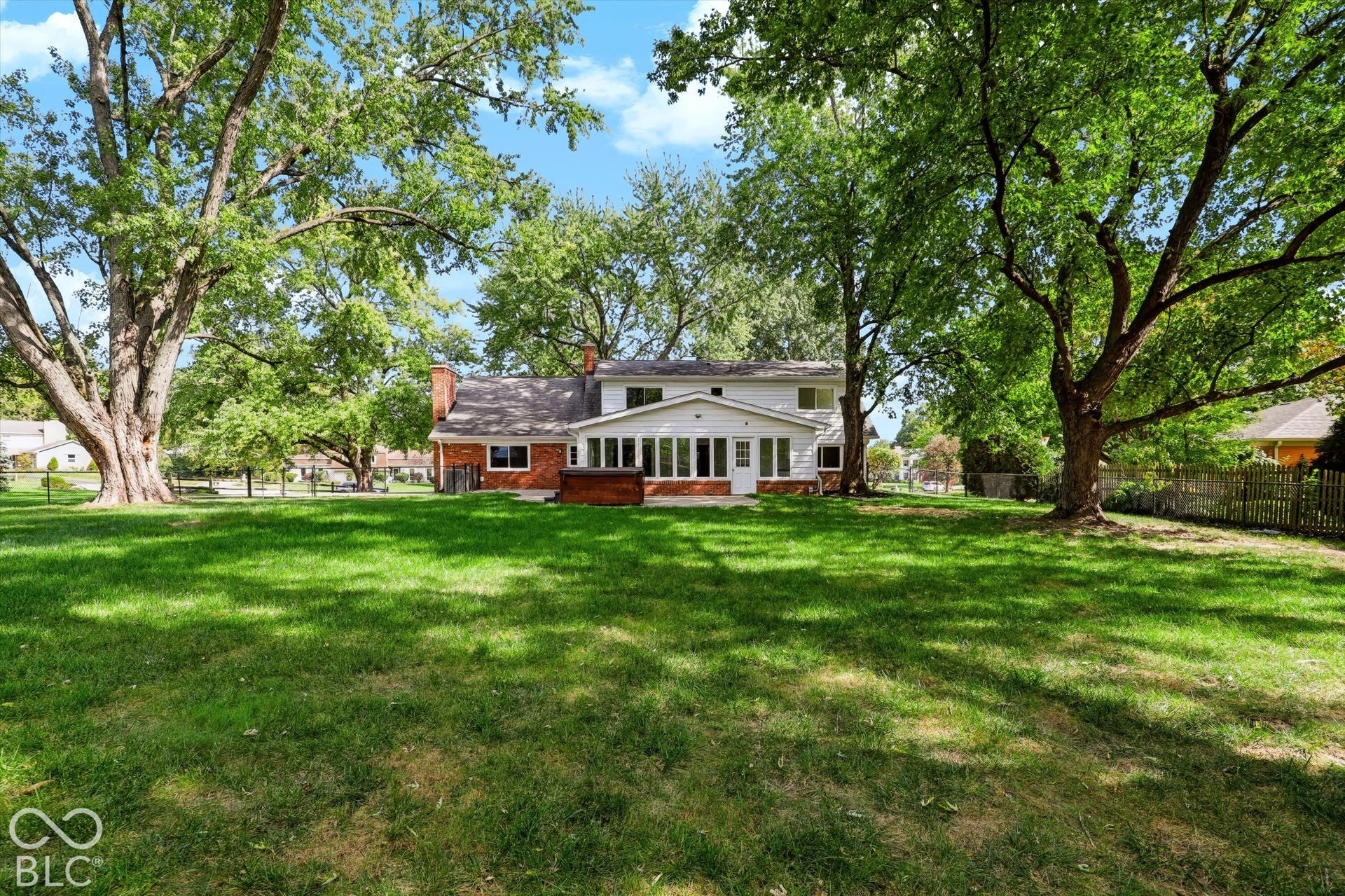 Expansive backyard featuring a large grass lawn, mature trees, brick and siding exterior, two exterior chimneys, and a built-in hot tub