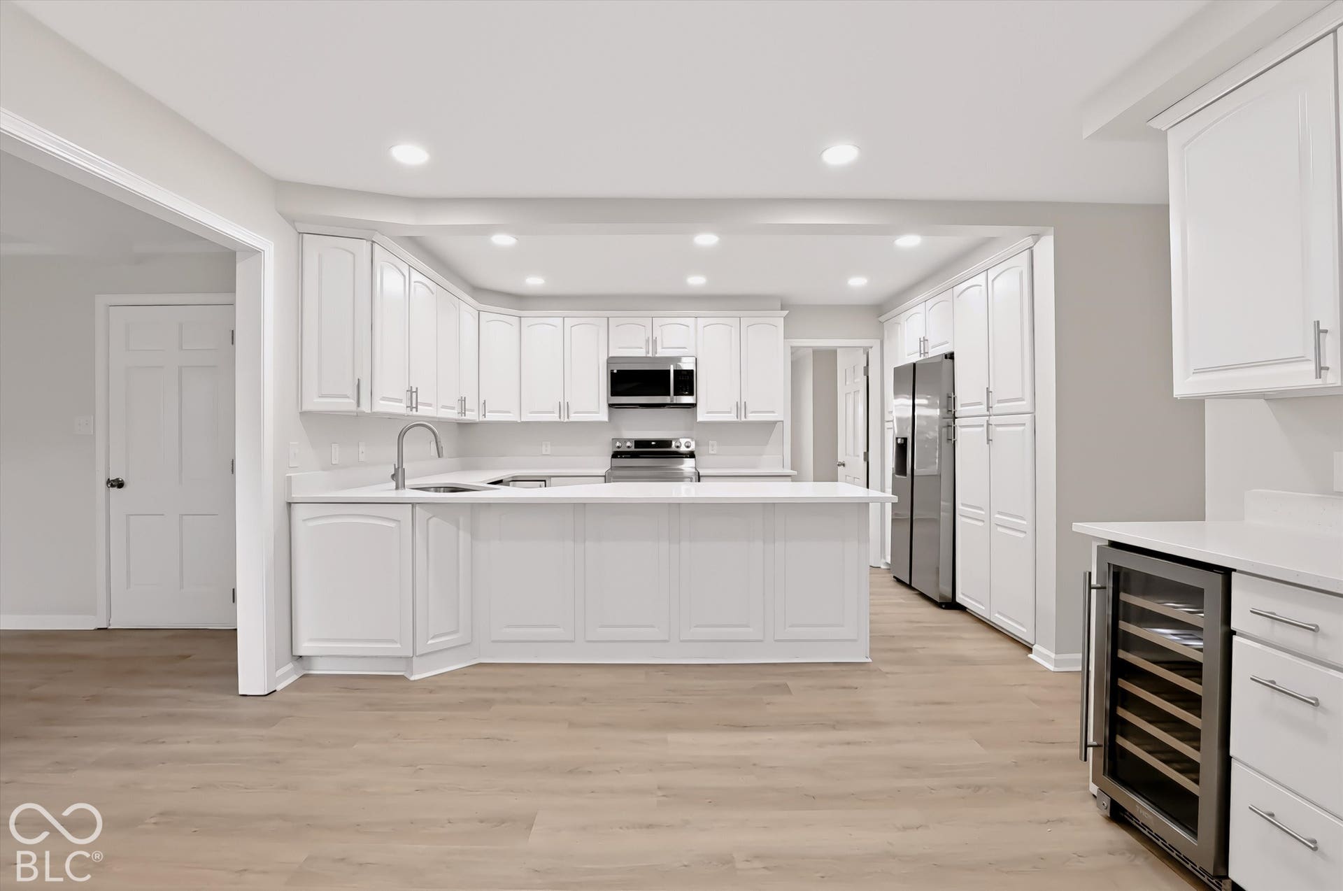 Kitchen featuring white shaker-style cabinetry, stainless steel appliances, a peninsula with stone-finish countertops, recessed lighting, and wood-finish flooring