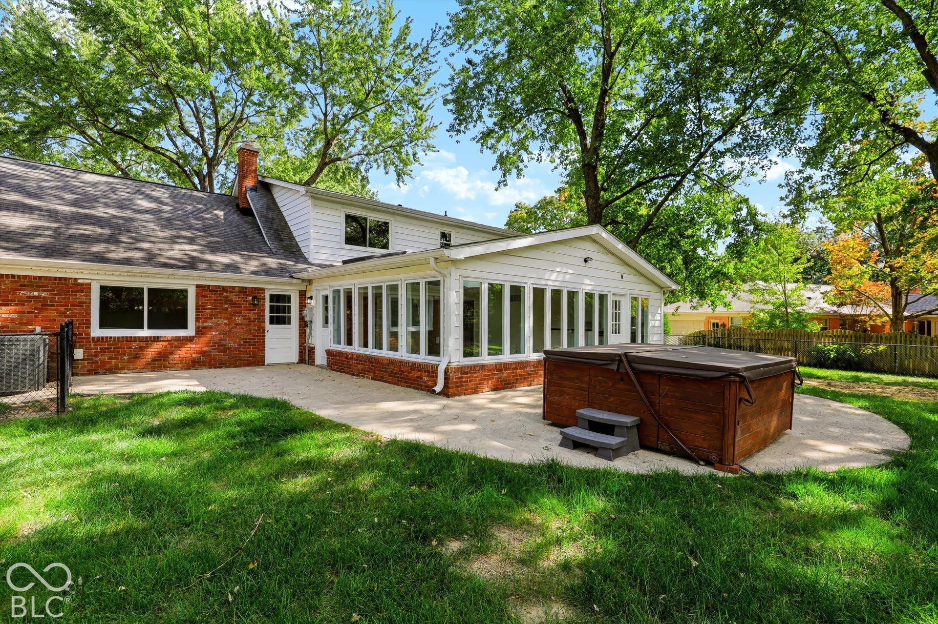 Rear exterior featuring a brick and siding facade, a sunroom with large windows, a concrete patio, and mature trees