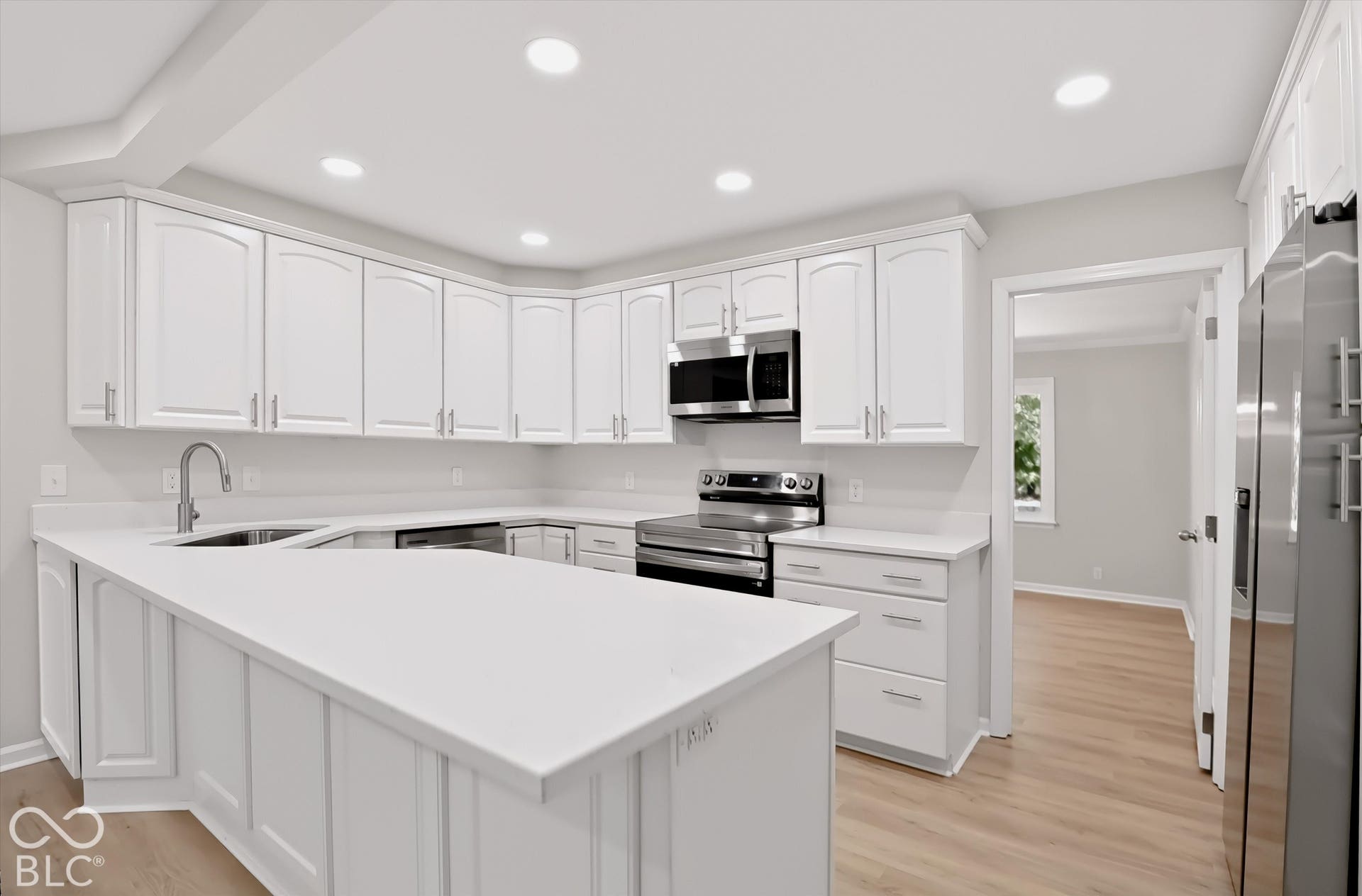 Kitchen featuring white cabinetry, solid surface countertops, stainless steel appliances, recessed lighting, and wood-finish flooring