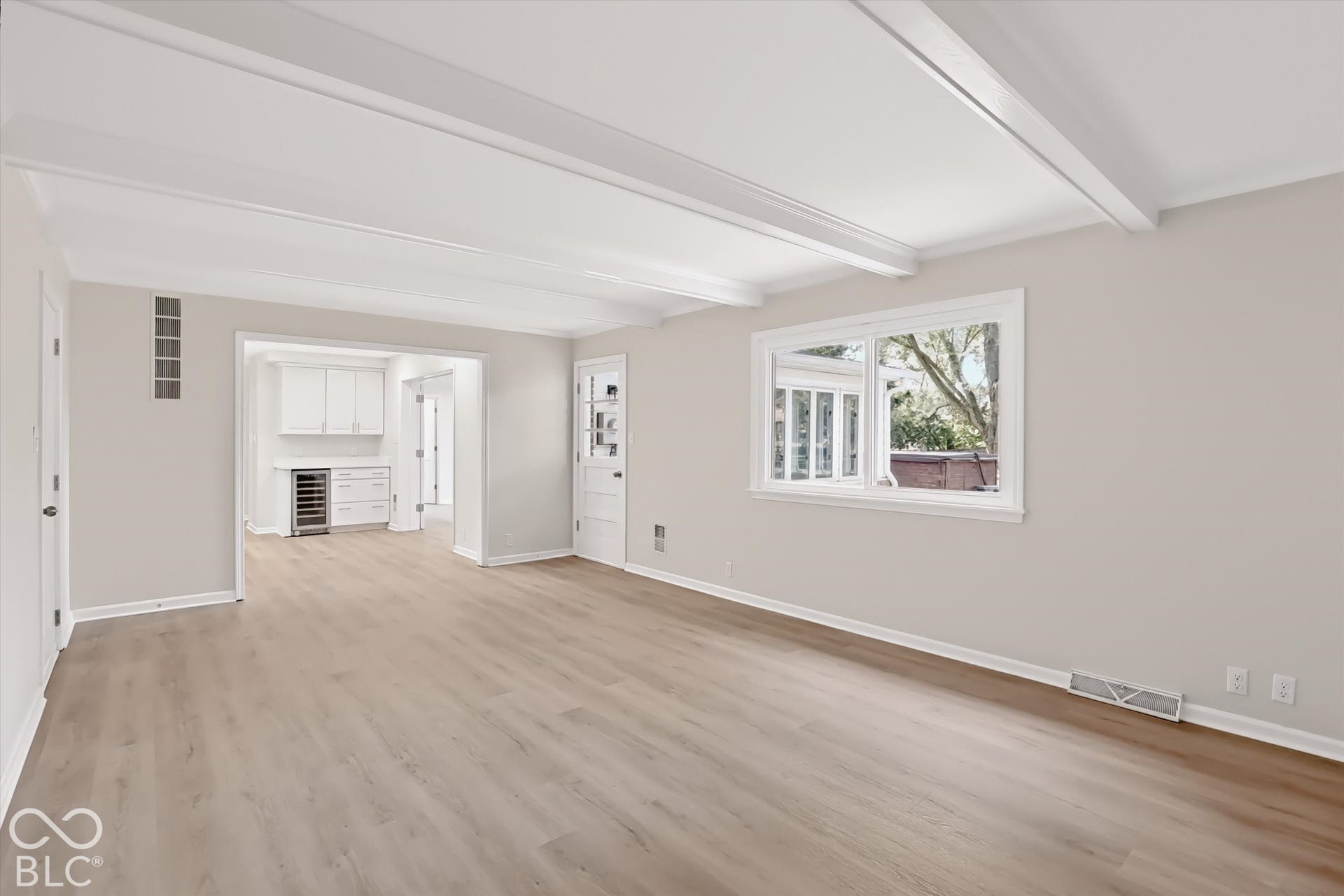 Living space featuring a white beamed ceiling, wood-finish flooring, a multi-pane glass door, and integrated cabinetry with a built-in wine cooler