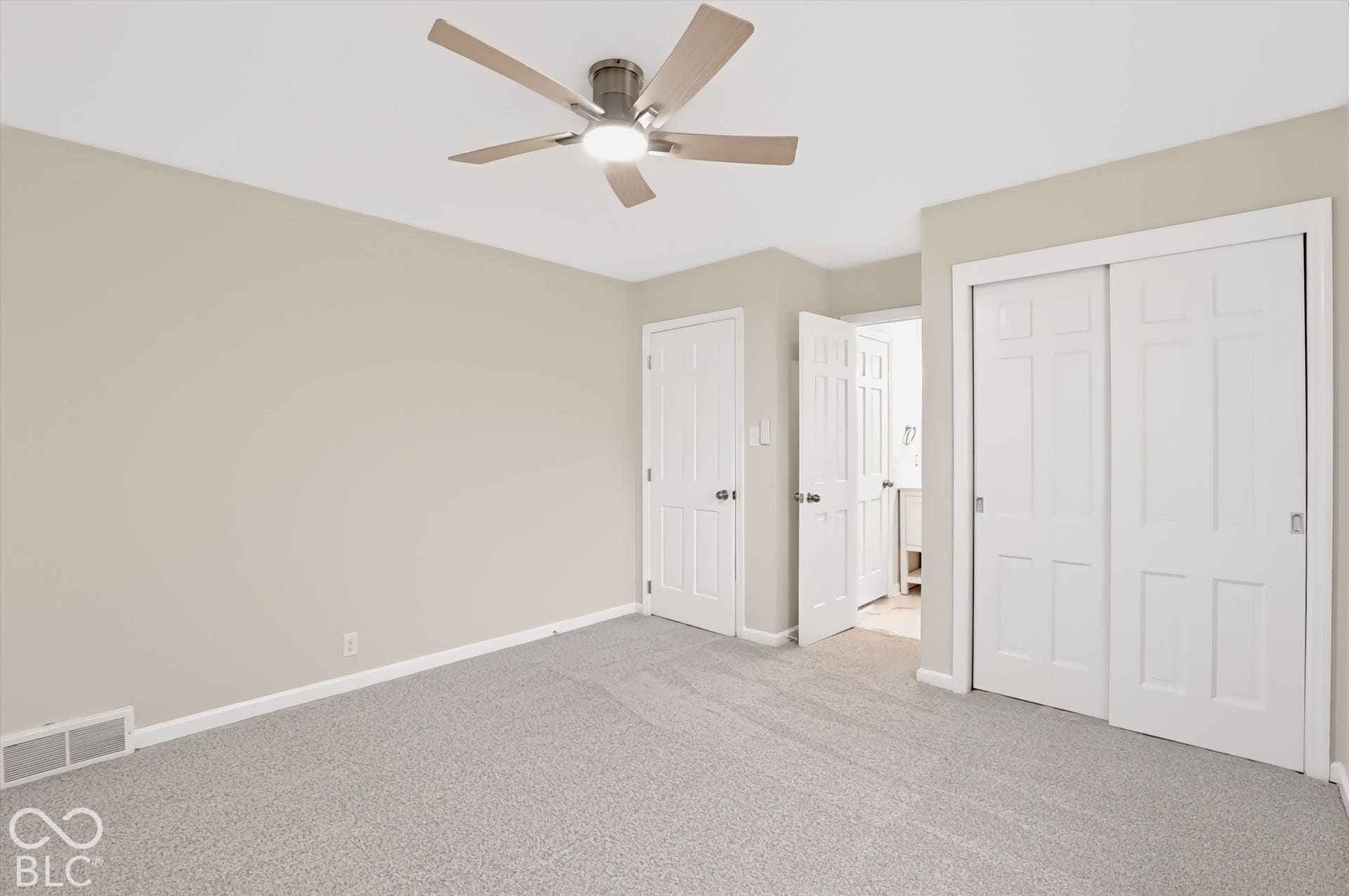 Neutral-toned interior space featuring neutral wall-to-wall carpeting, a multi-blade ceiling fan with integrated lighting, and white six-panel interior doors