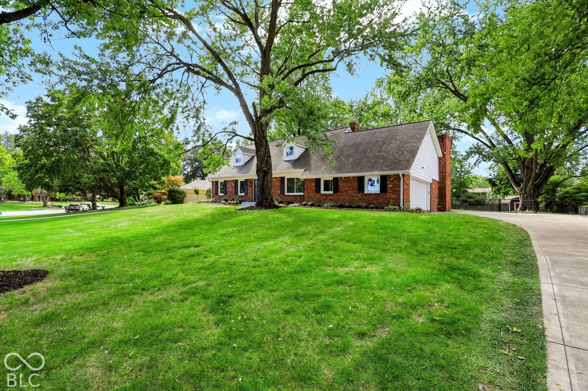 Traditional brick exterior featuring a steeply pitched roof, dormer windows, a side-entry garage, and a sprawling lawn with mature trees
