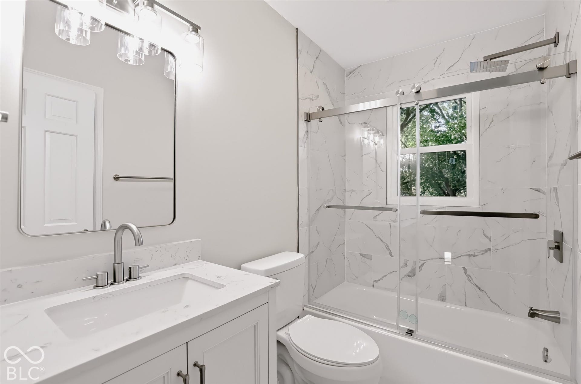 Bathroom featuring a vanity with a stone-surface countertop, rectangular undermount sink, and arched-frame mirror