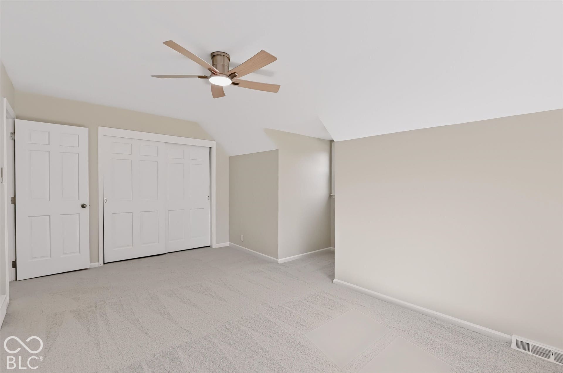 Room featuring neutral wall tones, carpeted flooring, a five-blade ceiling fan with integrated lighting, and a multi-panel interior door with sliding-panel closet doors