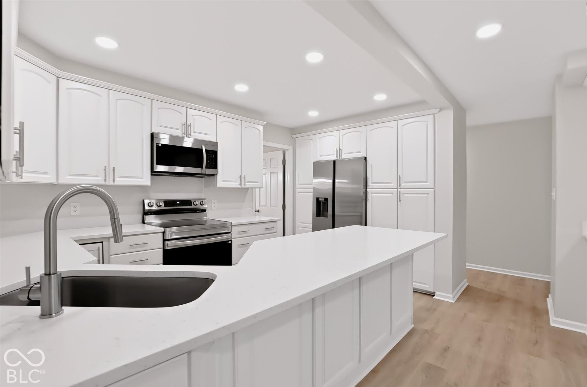 Kitchen featuring white cabinetry, solid-surface countertops, stainless steel appliances, a peninsula with an undermount sink, and wood-finish flooring