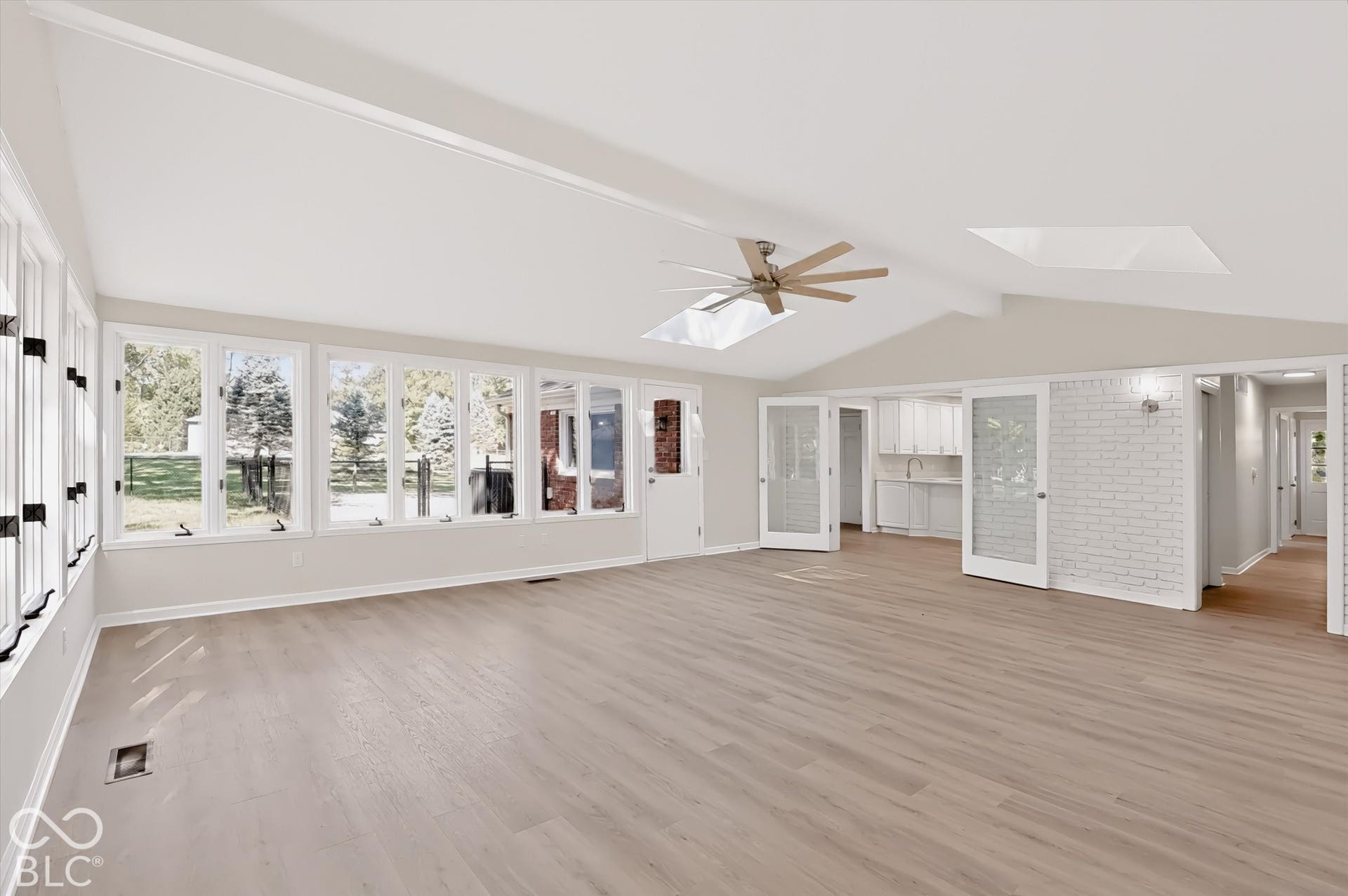 Vaulted ceiling interior featuring wood-finish flooring, white brick accent wall, multiple skylights, and extensive window groupings