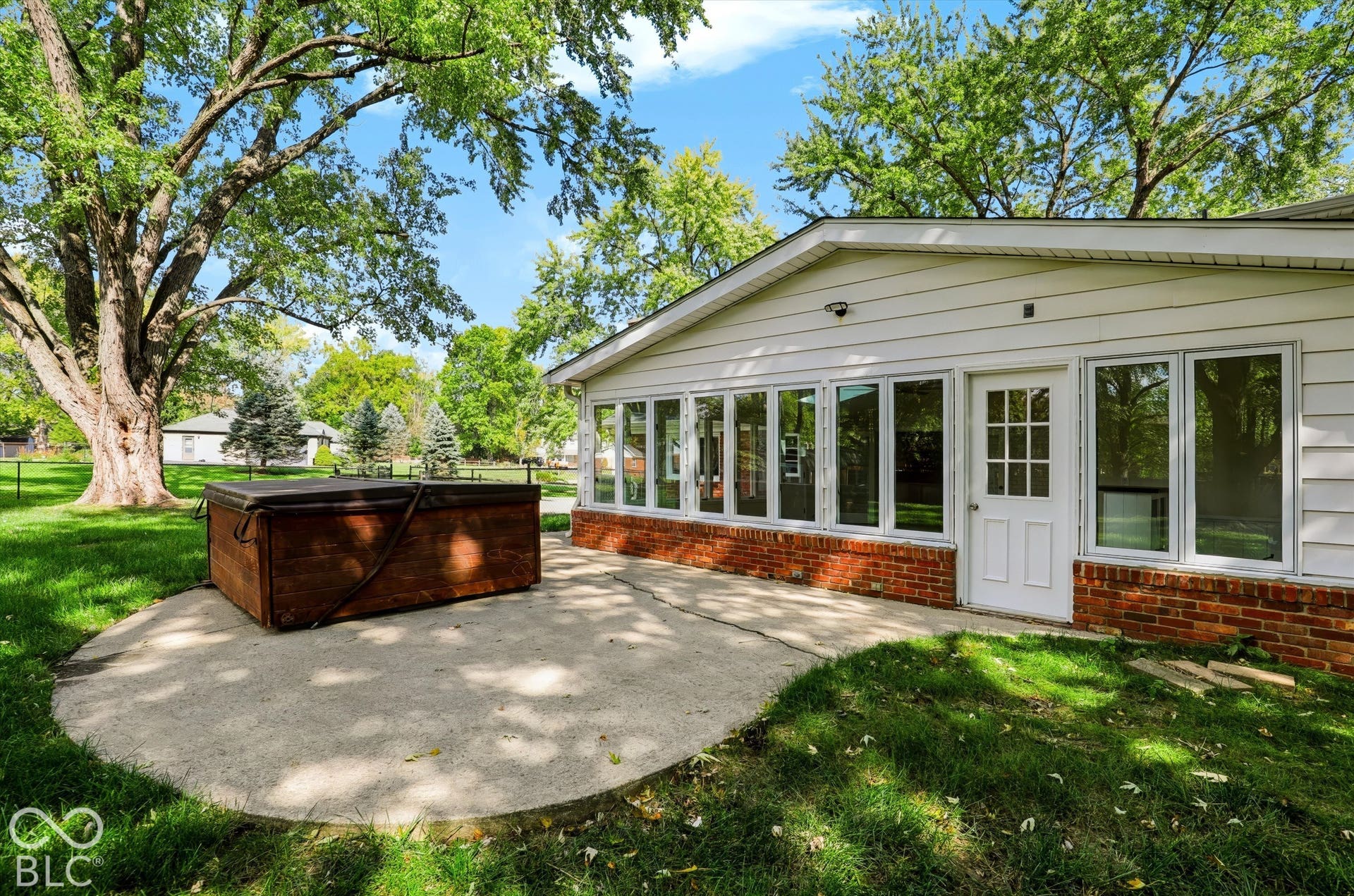 Rear exterior featuring a concrete patio, red brick foundation, horizontal lap siding, and expansive windows