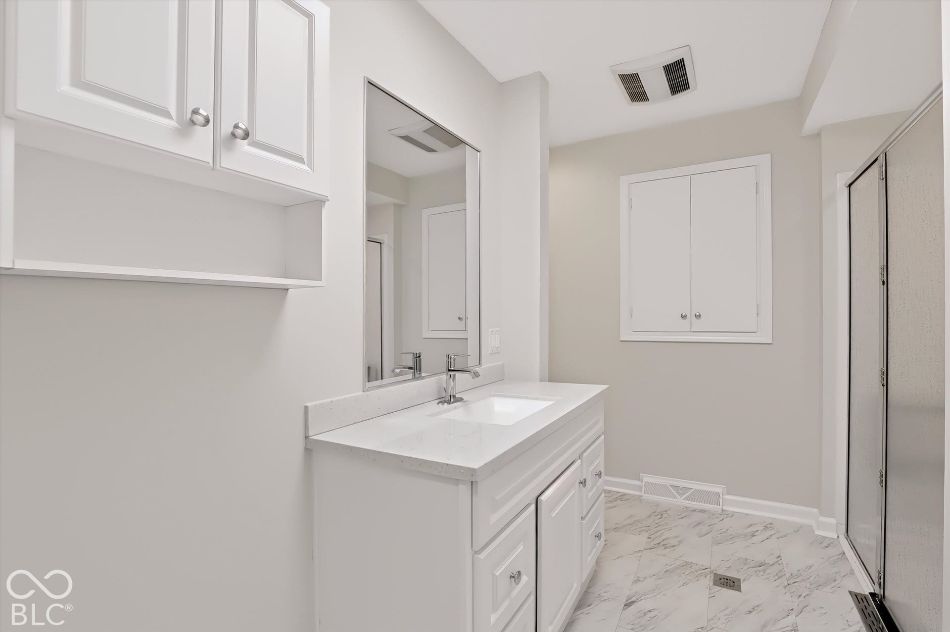 White vanity featuring a solid surface countertop, rectangular under-mount sink, integrated cabinetry with silver-tone hardware, and a frameless wall mirror