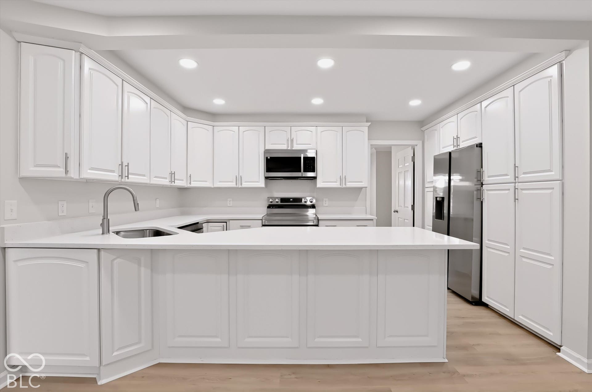Kitchen featuring white cabinetry, solid-surface countertops, stainless steel appliances, recessed ceiling lighting, and wood-finish flooring