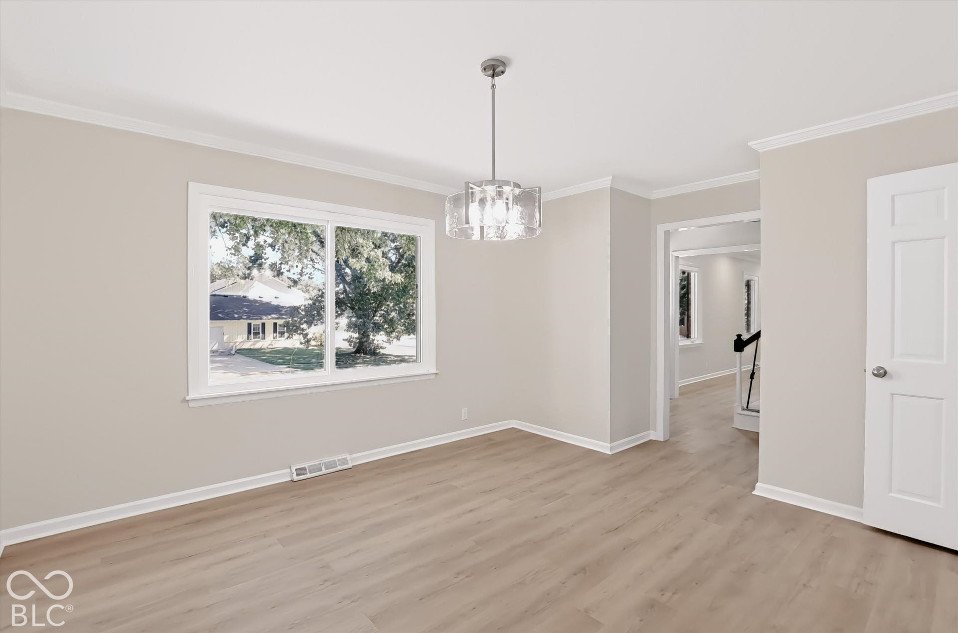 Neutral wall tones, wood-finish flooring, crown molding, and a contemporary multi-light metal pendant fixture