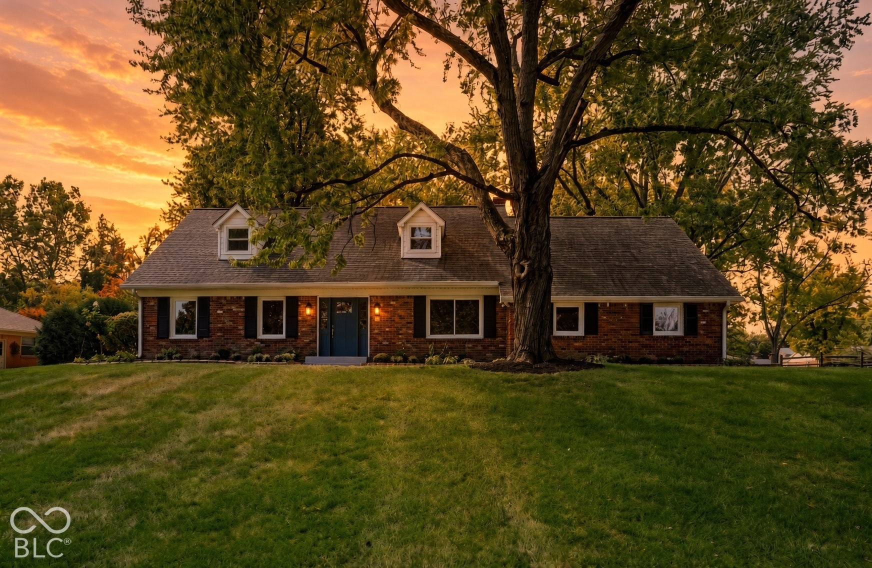 Virtually Altered - Brick exterior residence featuring a gabled roof, dual dormer windows, shutters, and a mature tree