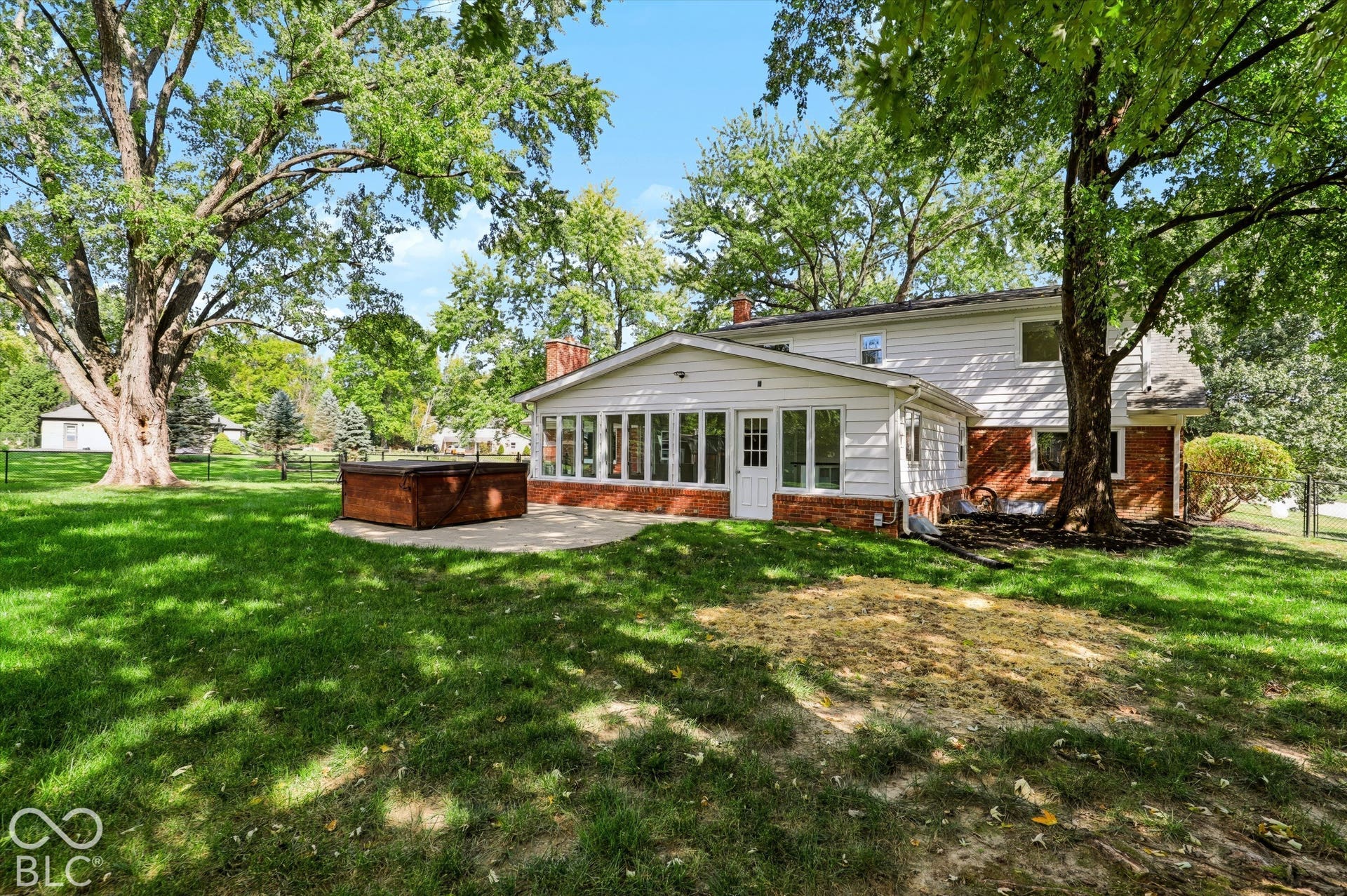 Backyard featuring an expansive lawn, mature trees, a detached hot tub, and a concrete patio