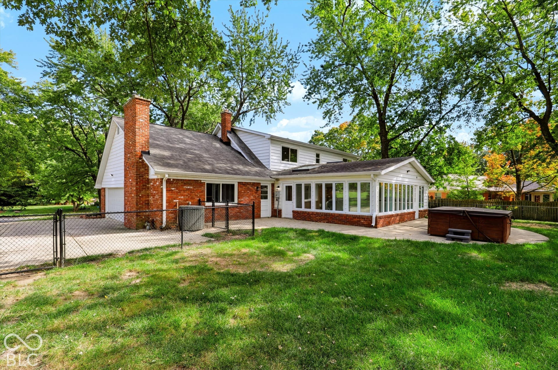 Exterior featuring a brick and white siding facade, a sunroom with large windows, a concrete patio, and mature trees