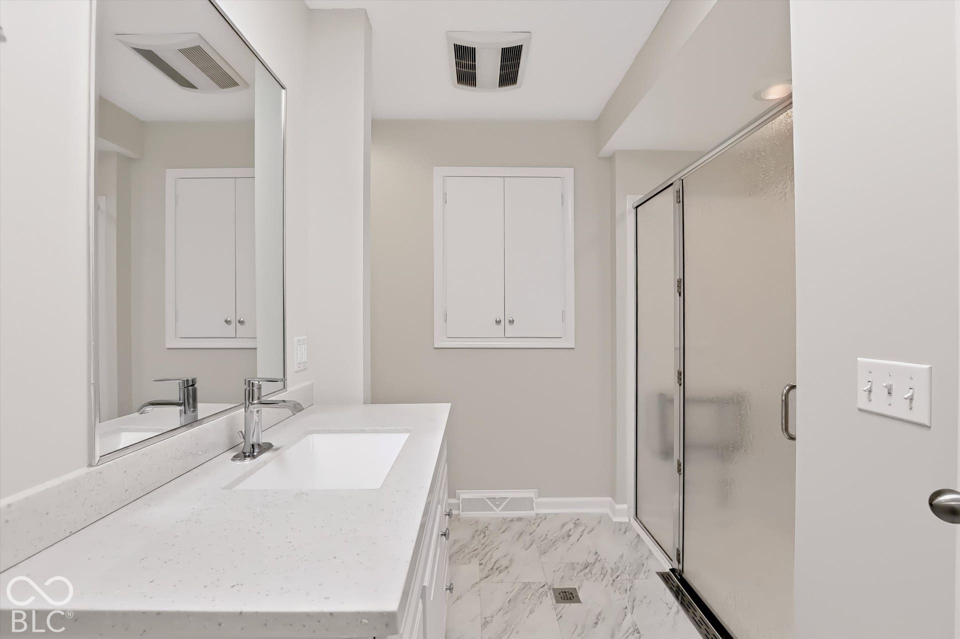 Bathroom featuring a vanity with a white countertop and rectangular undermount sink, stone-finish flooring, a frameless glass-enclosed shower, and built-in wall cabinetry