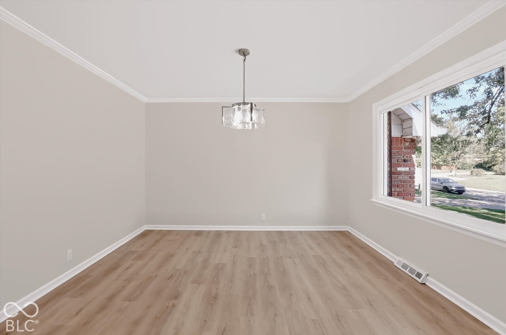 Neutral-toned walls, wood-finish flooring, multi-pane glass chandelier, crown molding, and large window