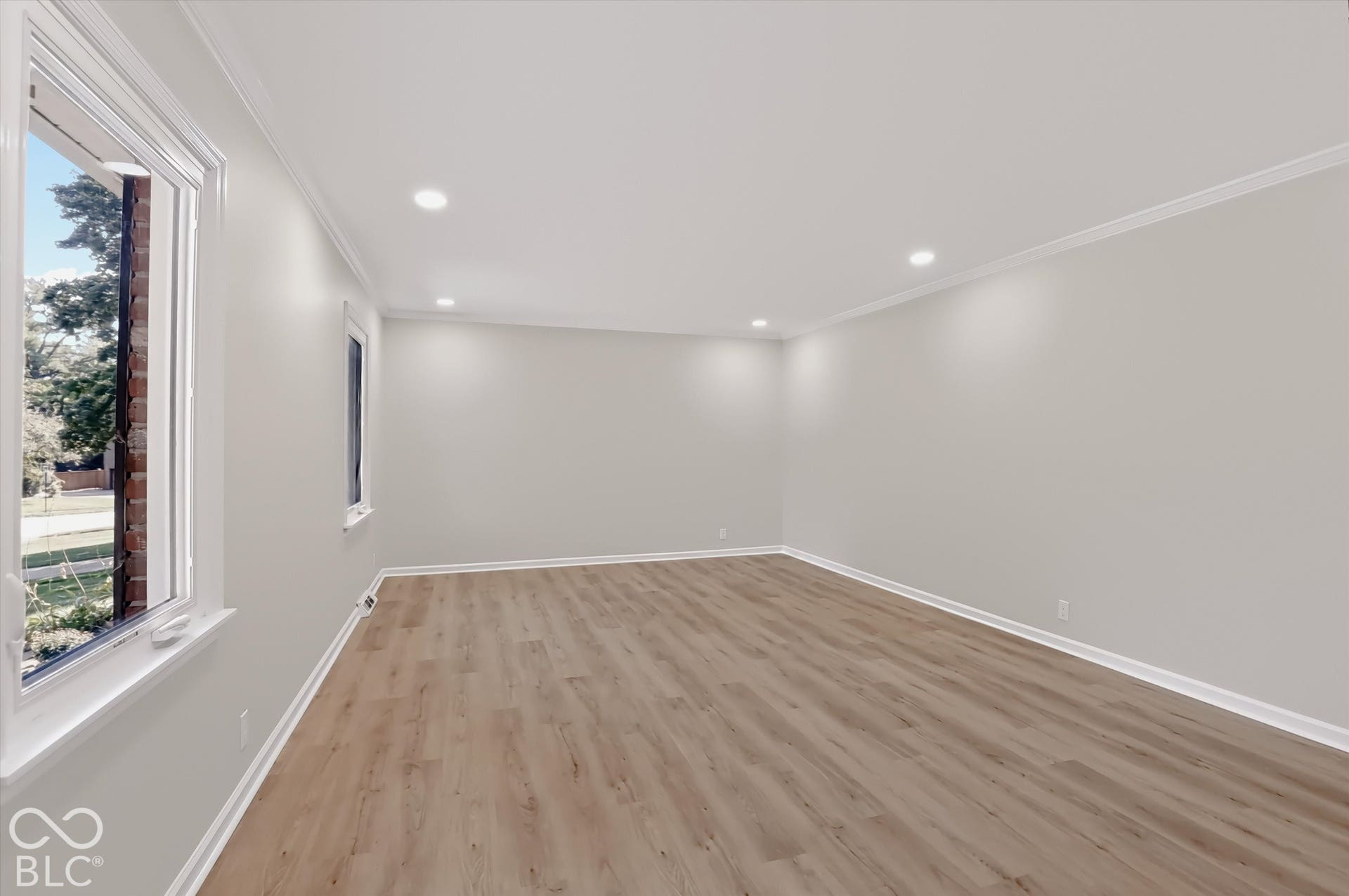 Neutral-toned interior space featuring wood-finish flooring, recessed lighting, crown molding, and large double-pane windows