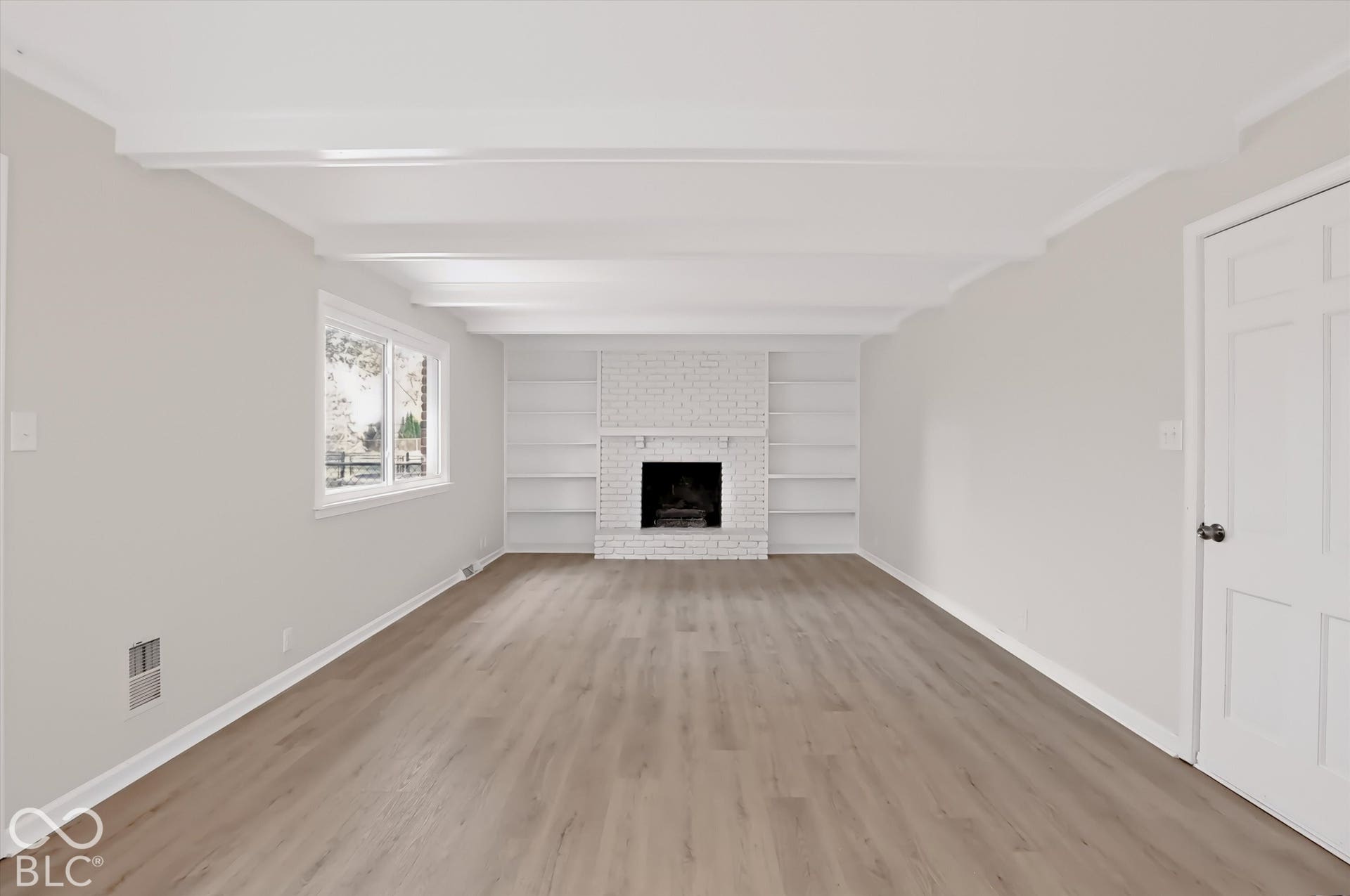 Living space featuring wood-finish flooring, white exposed ceiling beams, a floor-to-ceiling painted brick fireplace, and built-in shelving