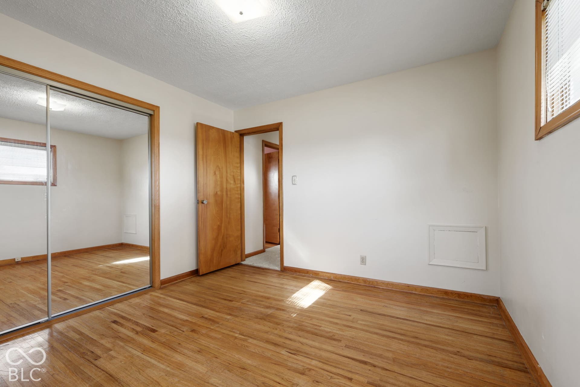 280 Anniston, Indianapolis, IN 46227 Room featuring wood-finish flooring, sliding mirror-paneled closet doors, solid wood doors with matching trim, and a window with horizontal blinds