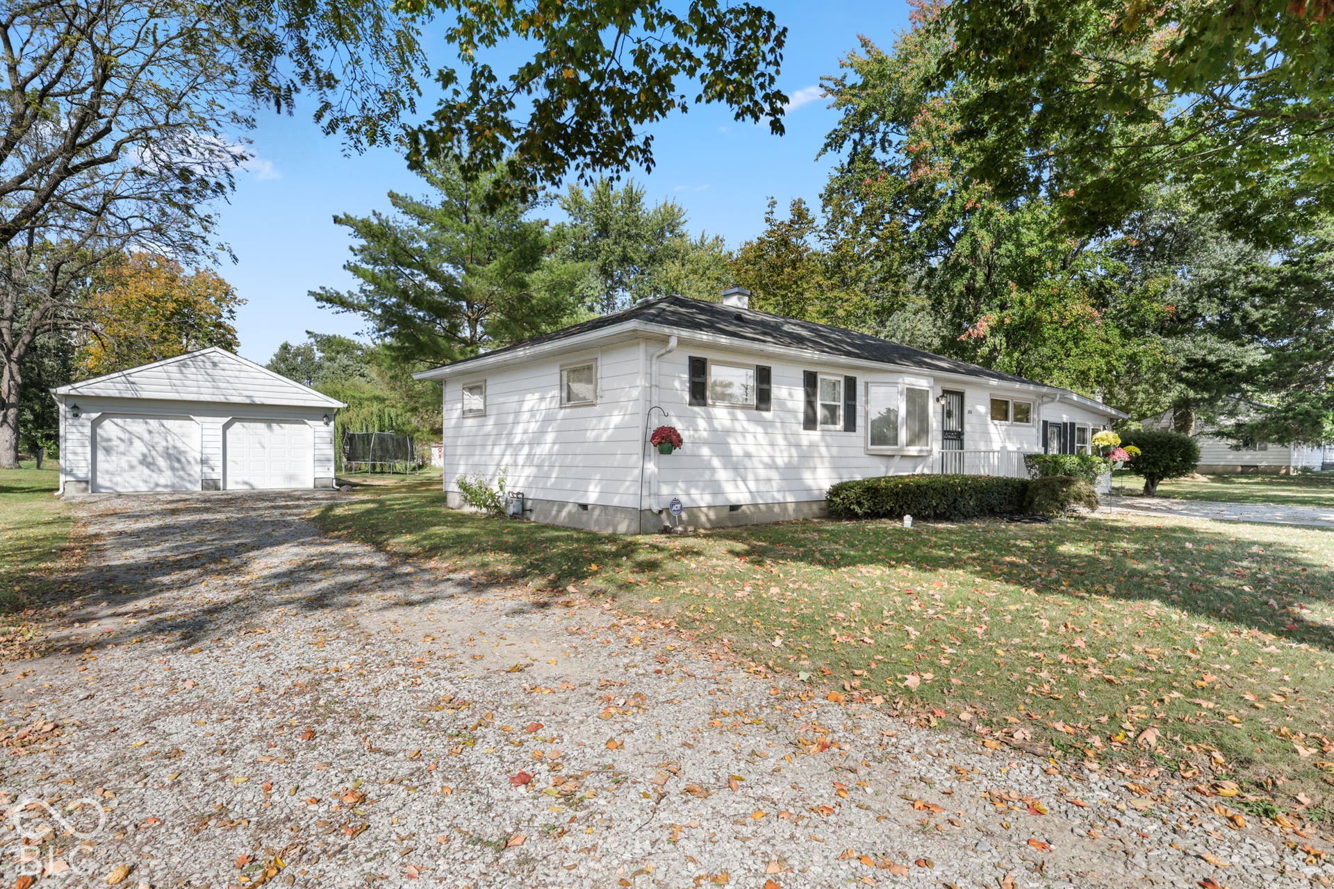 280 Anniston, Indianapolis, IN 46227 Single-story exterior featuring white horizontal siding, a detached two-car garage, and a gravel driveway set on a tree-lined lot