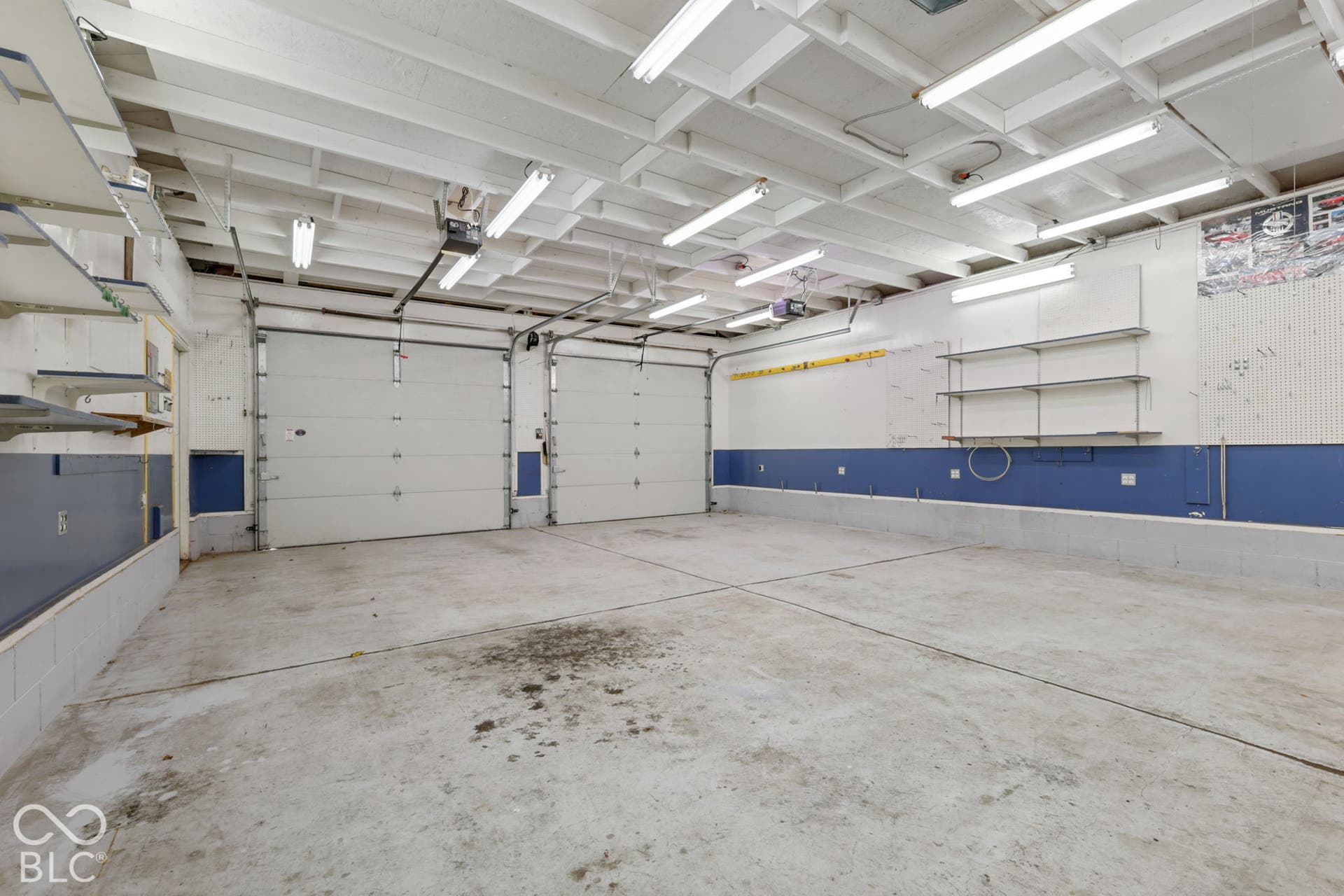 280 Anniston, Indianapolis, IN 46227 Two-car garage featuring concrete flooring, exposed ceiling rafters, multiple overhead fluorescent lights, and wall-mounted metal shelving units