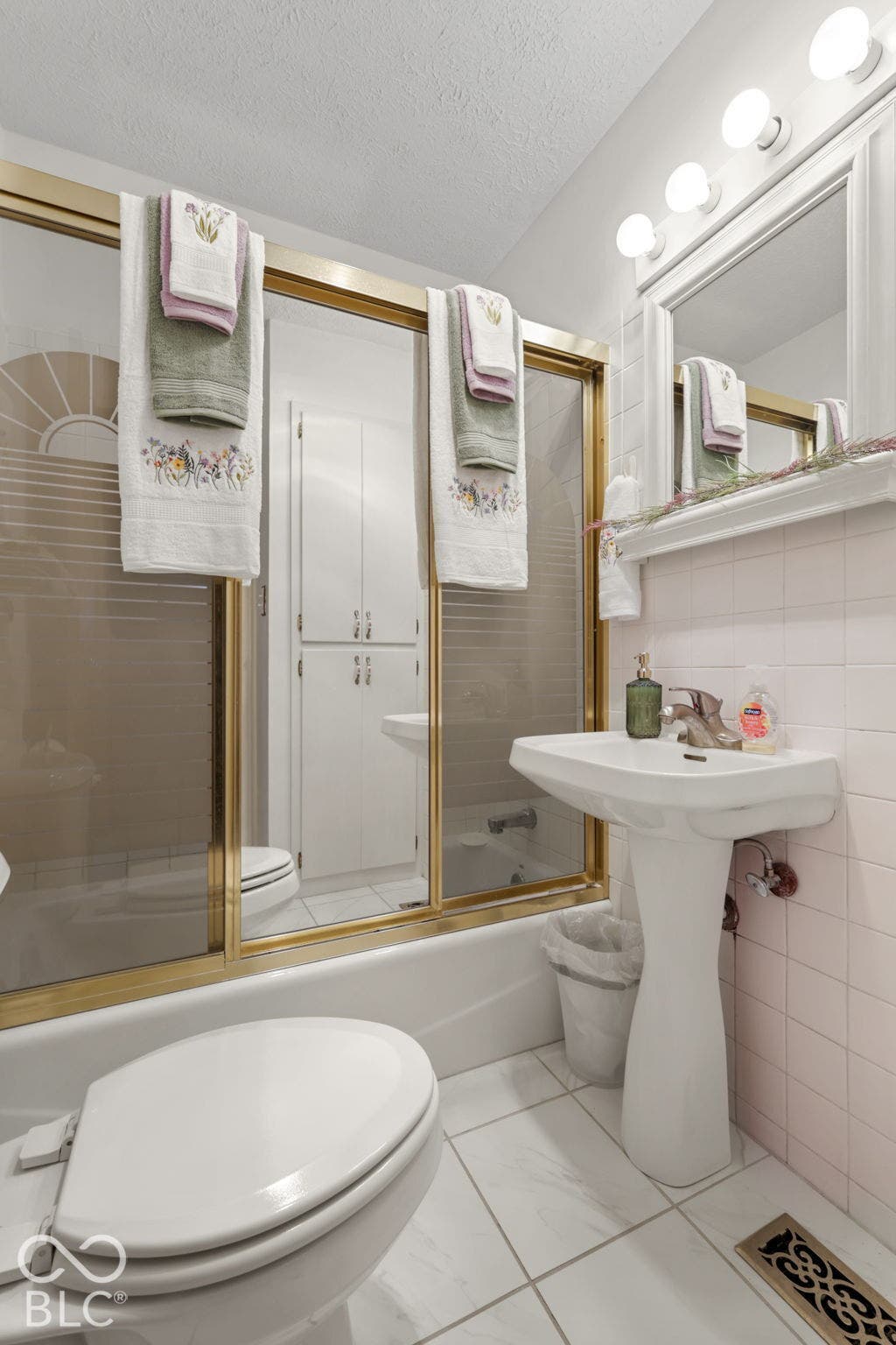 280 Anniston, Indianapolis, IN 46227 Pedestal sink with a single-handle faucet, wall-mounted mirror with decorative lighting, tub-shower combination featuring metal-framed sliding doors, tiled wall surfacing, and built-in floor-to-ceiling storage cabinetry