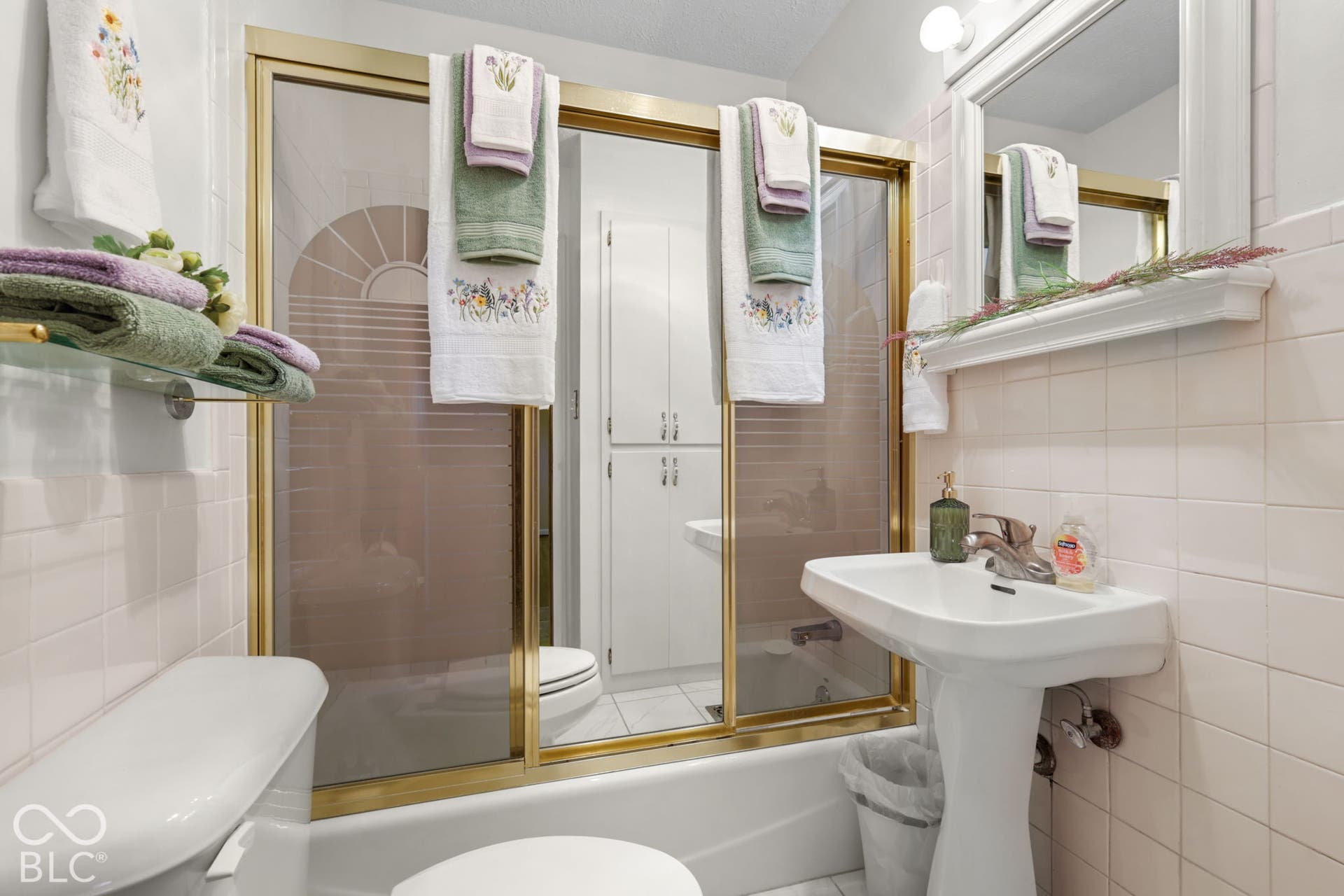 280 Anniston, Indianapolis, IN 46227 Bathroom featuring a pedestal sink, wall-mounted mirror with integrated shelf, tiled walls, and a tub-shower combination enclosed by sliding doors with brass-tone hardware