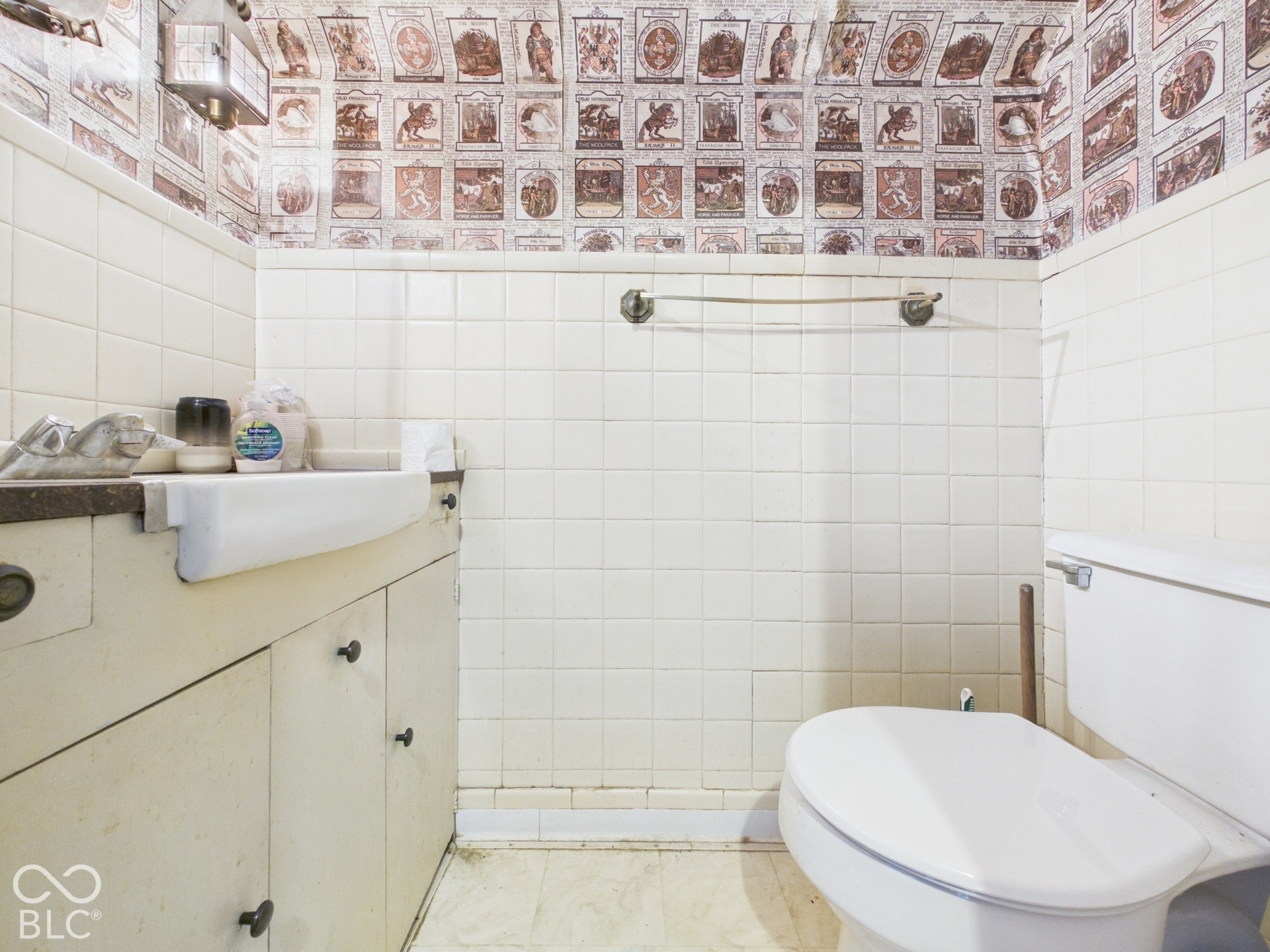 Wall-mounted sink with built-in cabinetry, ceramic tile wainscoting, and metallic towel bar