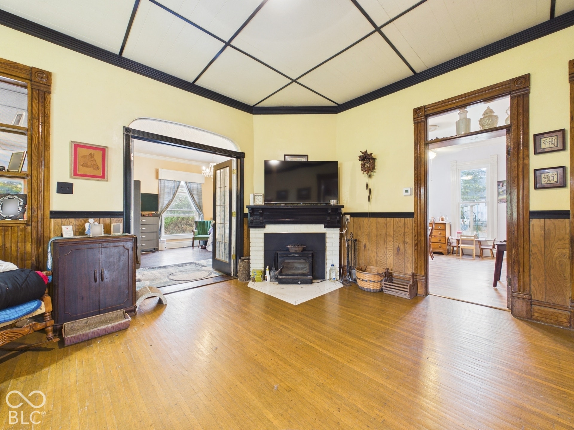 Wood-finish flooring, paneled walls, ceiling grid detailing, and a fireplace with a black mantel and tiled hearth