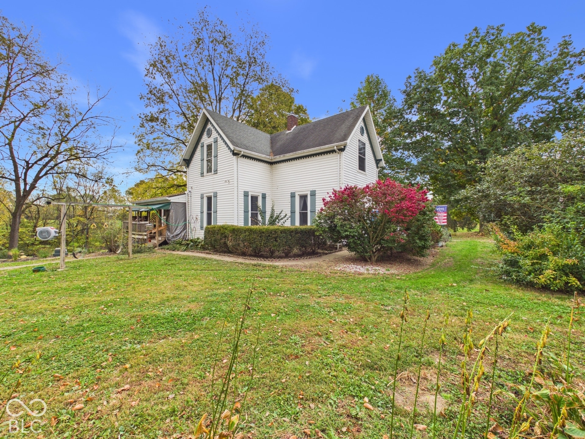 Two-story residence featuring white horizontal siding, gabled rooflines, decorative shutters, and expansive exterior grounds with mature trees