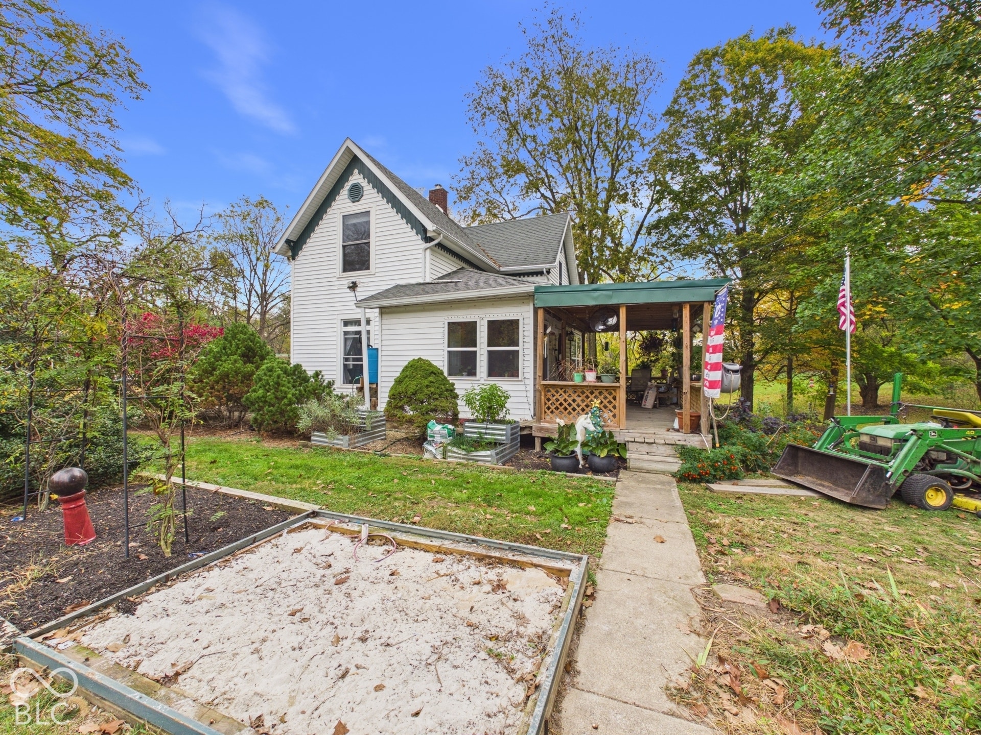 Exterior featuring white siding, a covered porch with lattice detail, a concrete walkway, and raised metal garden beds