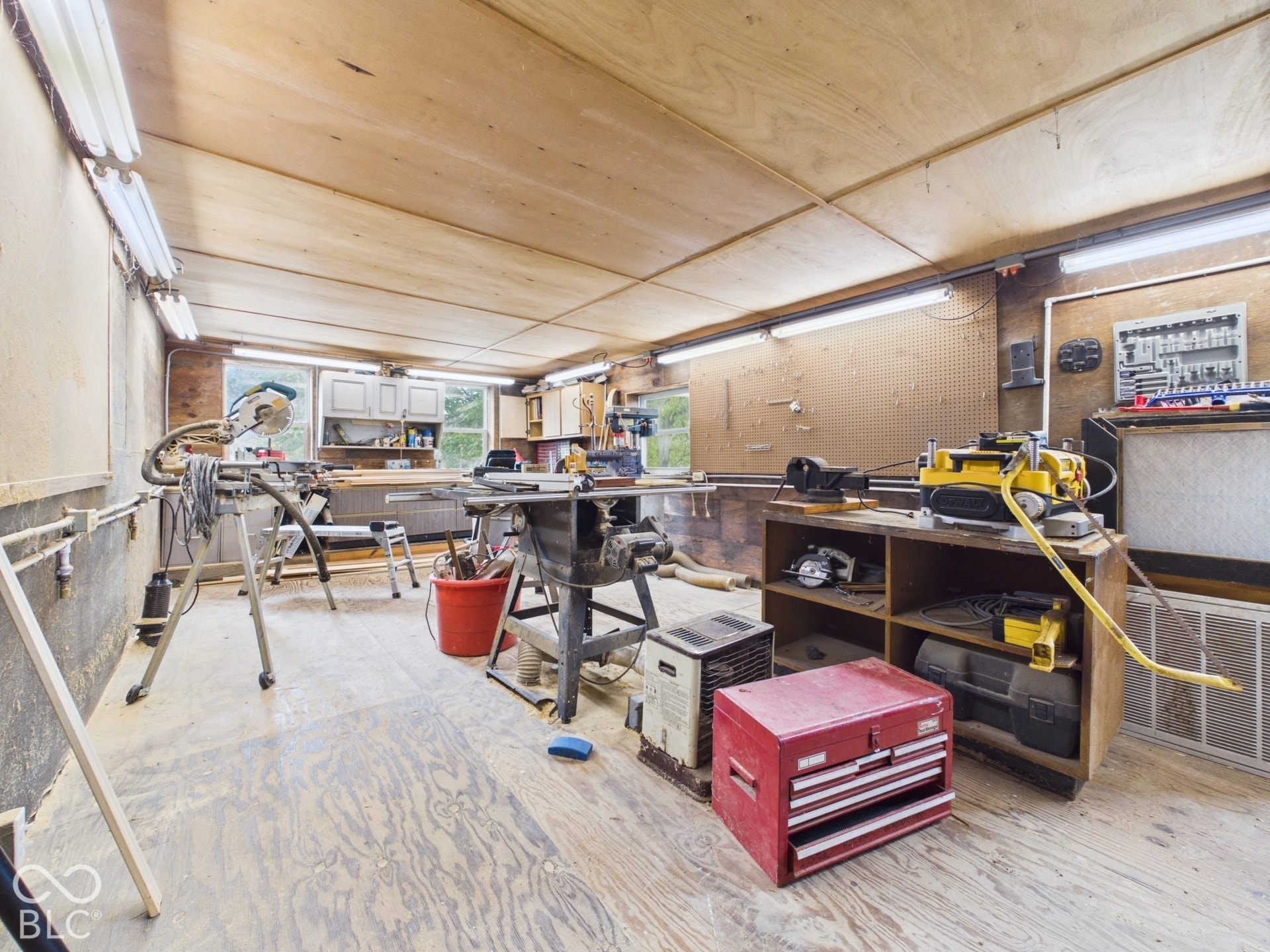 Workshop space featuring wood-paneled walls and ceiling, built-in cabinetry, integrated pegboard wall organizer, and fluorescent tube lighting