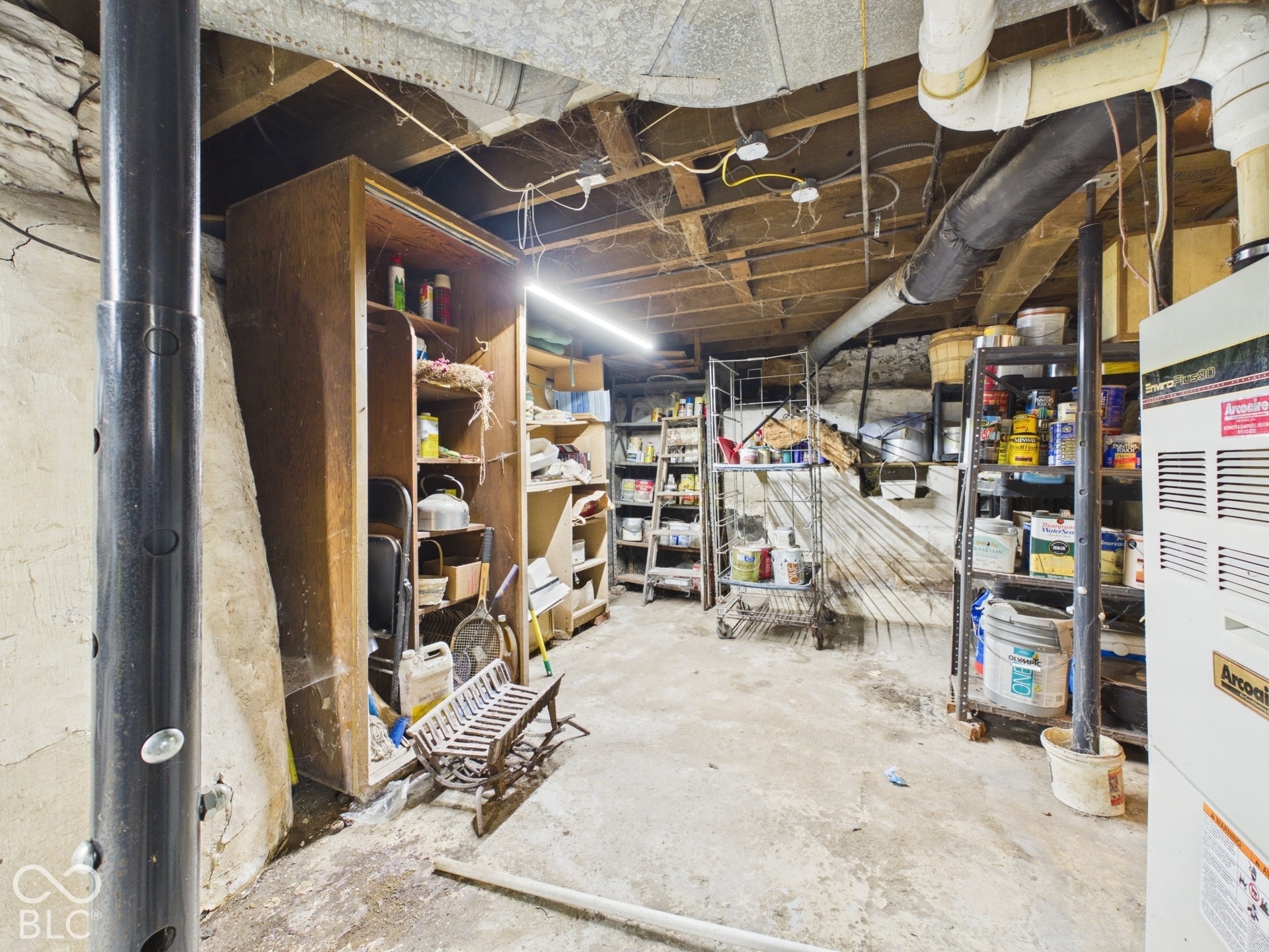 Unfinished basement with concrete flooring, stone foundation walls, exposed ceiling joists, and structural steel support columns