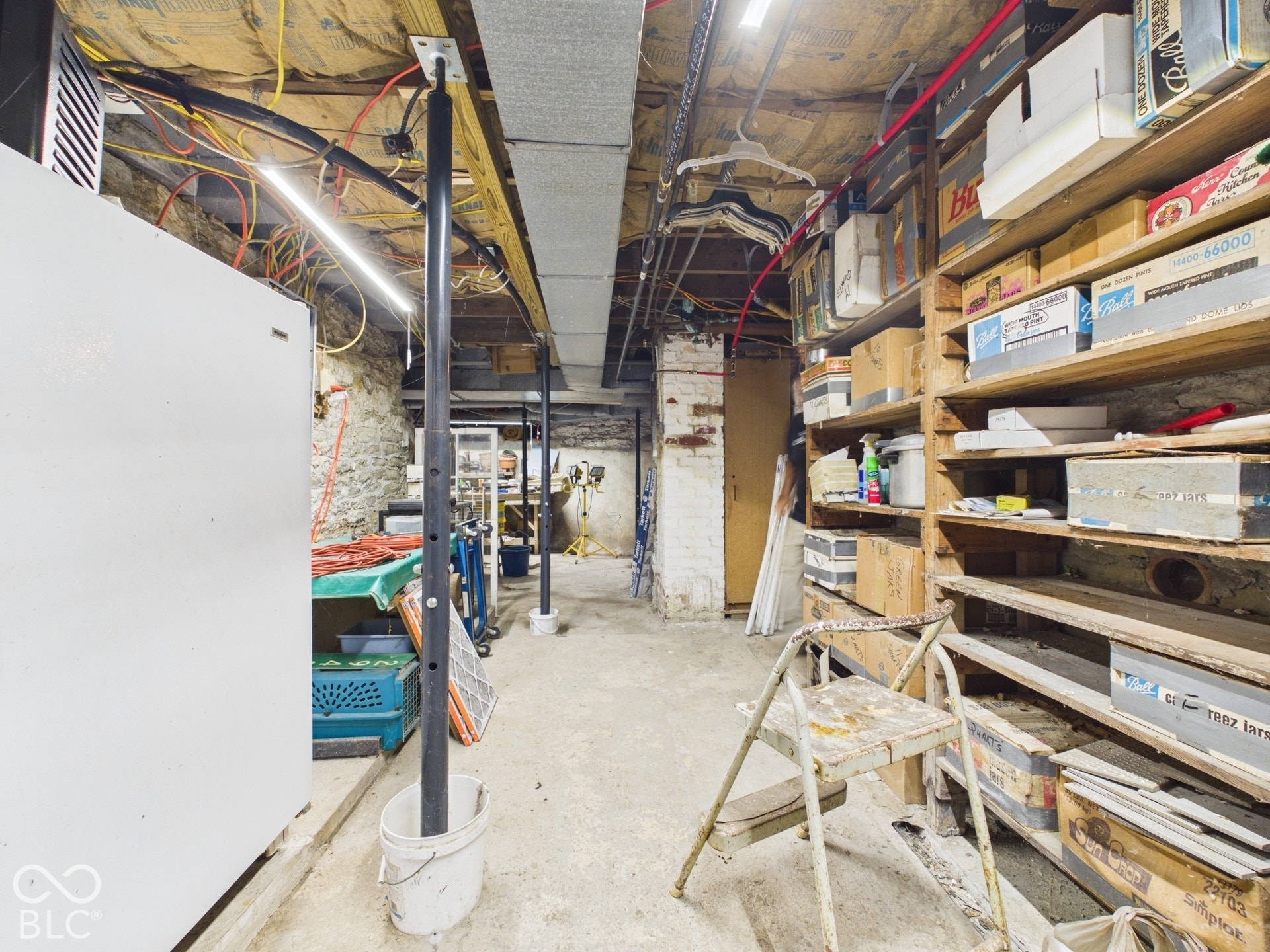 Unfinished basement featuring stone foundation walls, painted masonry column, concrete flooring, and built-in wood shelving units