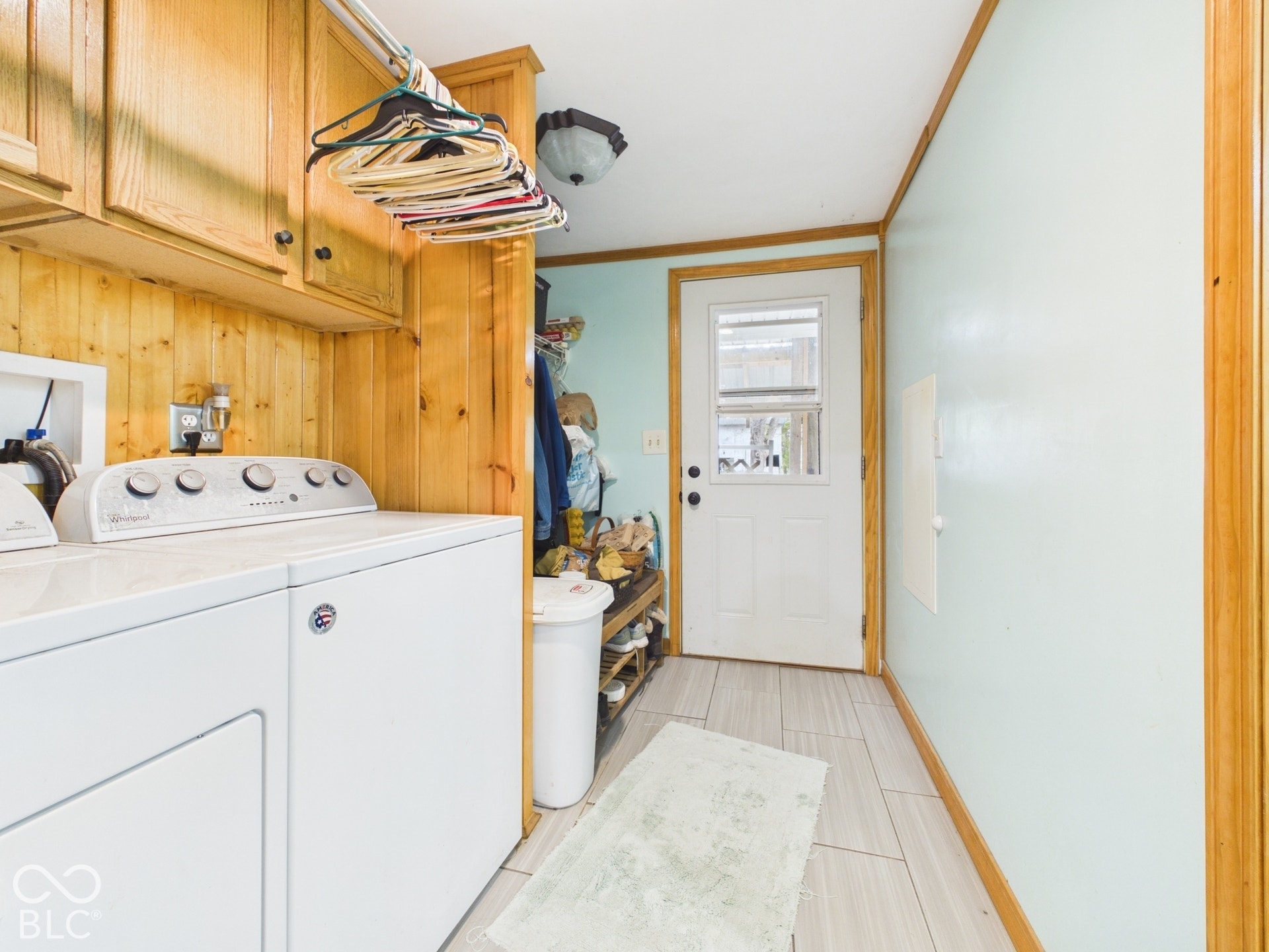 Utility space featuring wood-panel wall accents, overhead cabinetry, wood-finish trim, tile flooring, and a glass-paneled exterior door