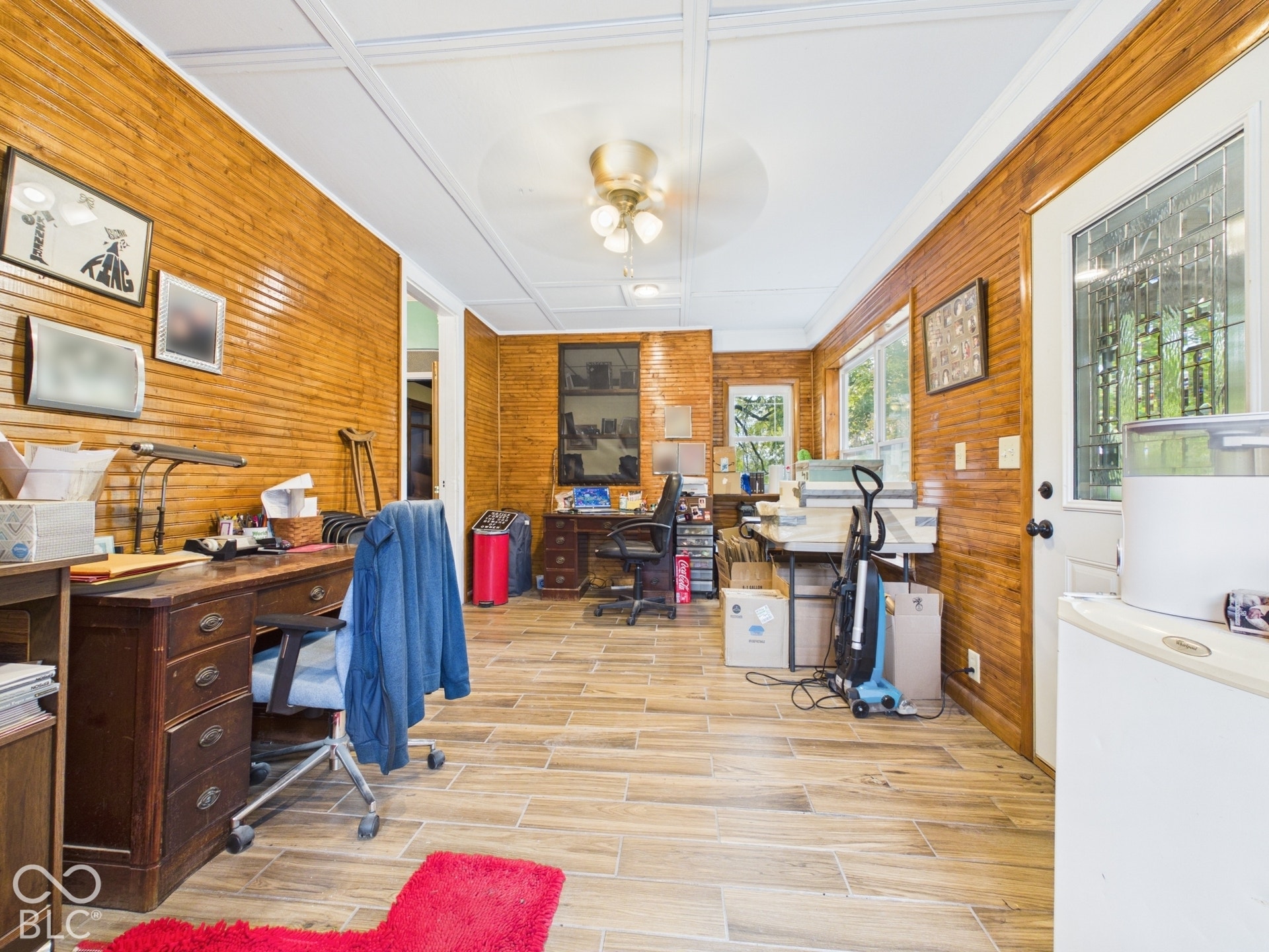 Interior room featuring horizontal wood wall paneling, tile flooring with a wood-finish, a coffered ceiling, a ceiling fan with light fixture, and an exterior door with glass insert