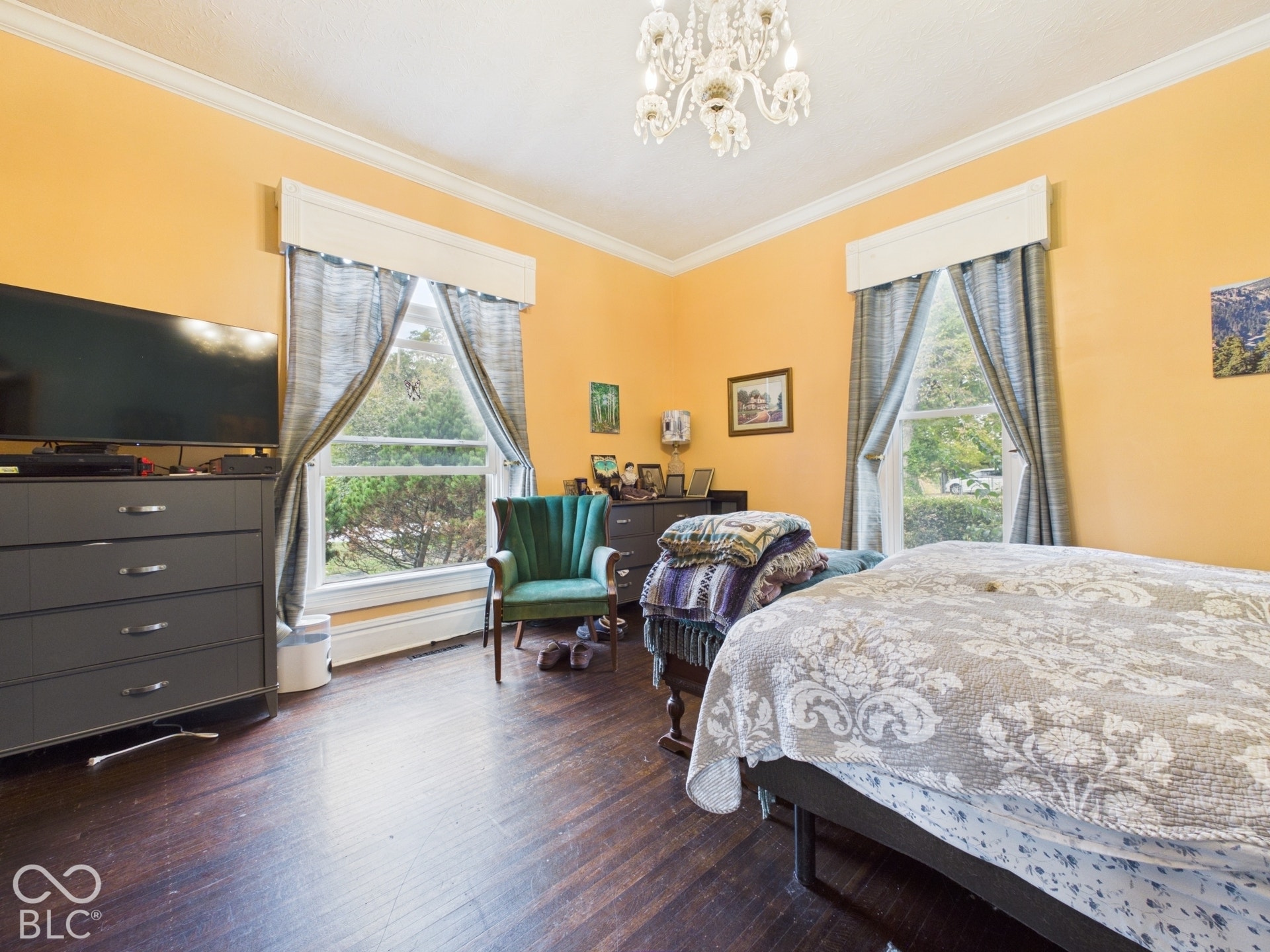 Room featuring wood-finish flooring, crown molding, two large windows with custom valances, and a decorative chandelier