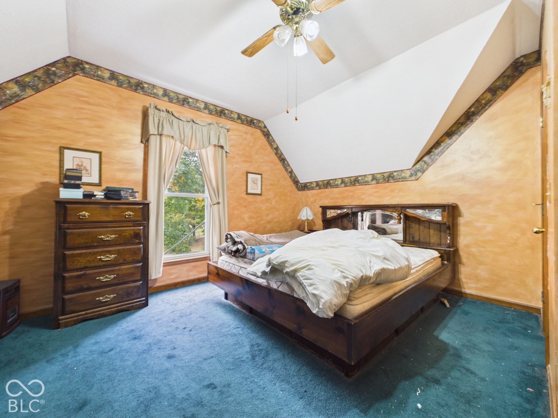 Vaulted ceiling featuring a central ceiling fan with multi-light fixture, dual-aspect wall angles, and window with exterior greenery