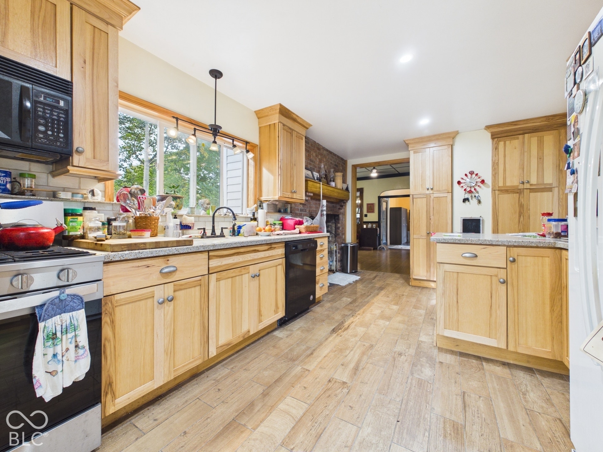 Kitchen featuring light-tone wood cabinetry, stone countertops, exposed brick chimney, wood-finish flooring, and recessed ceiling lighting