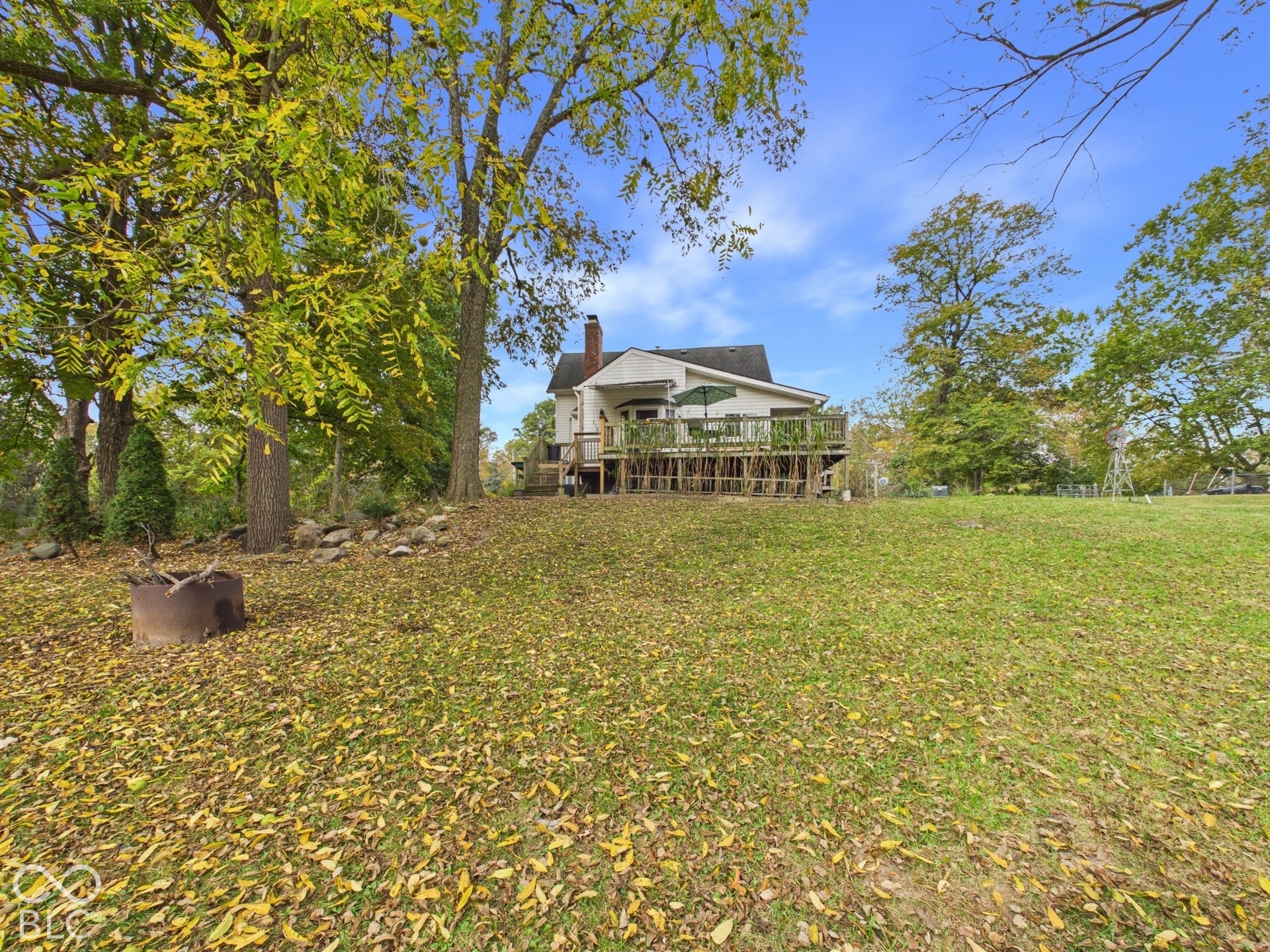 Expansive sloped backyard featuring mature trees, a wood deck with railings, and a brick chimney