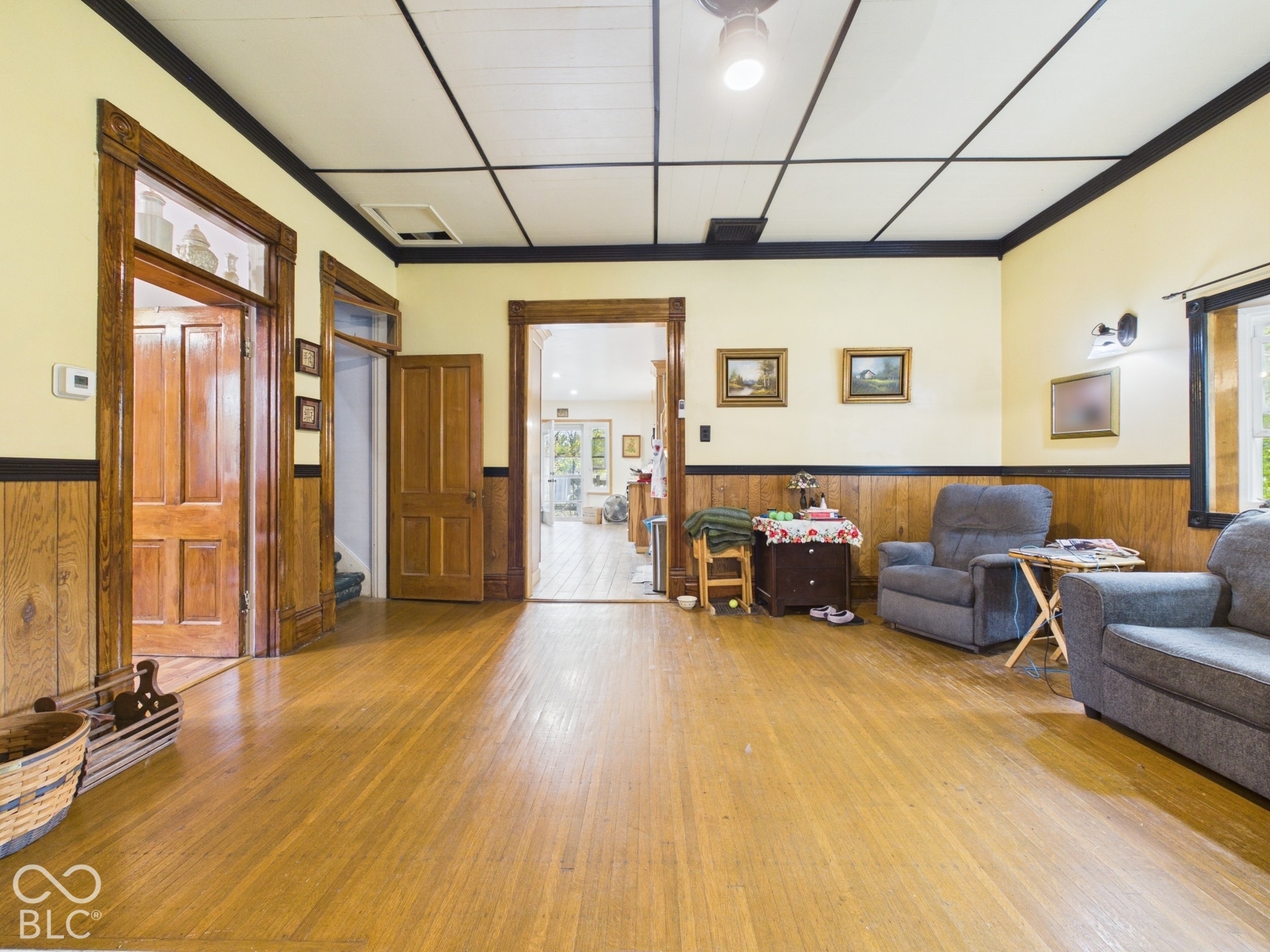 Hardwood flooring, natural wood trim, paneled wainscoting, grid-pattern ceiling, and solid wood interior doors
