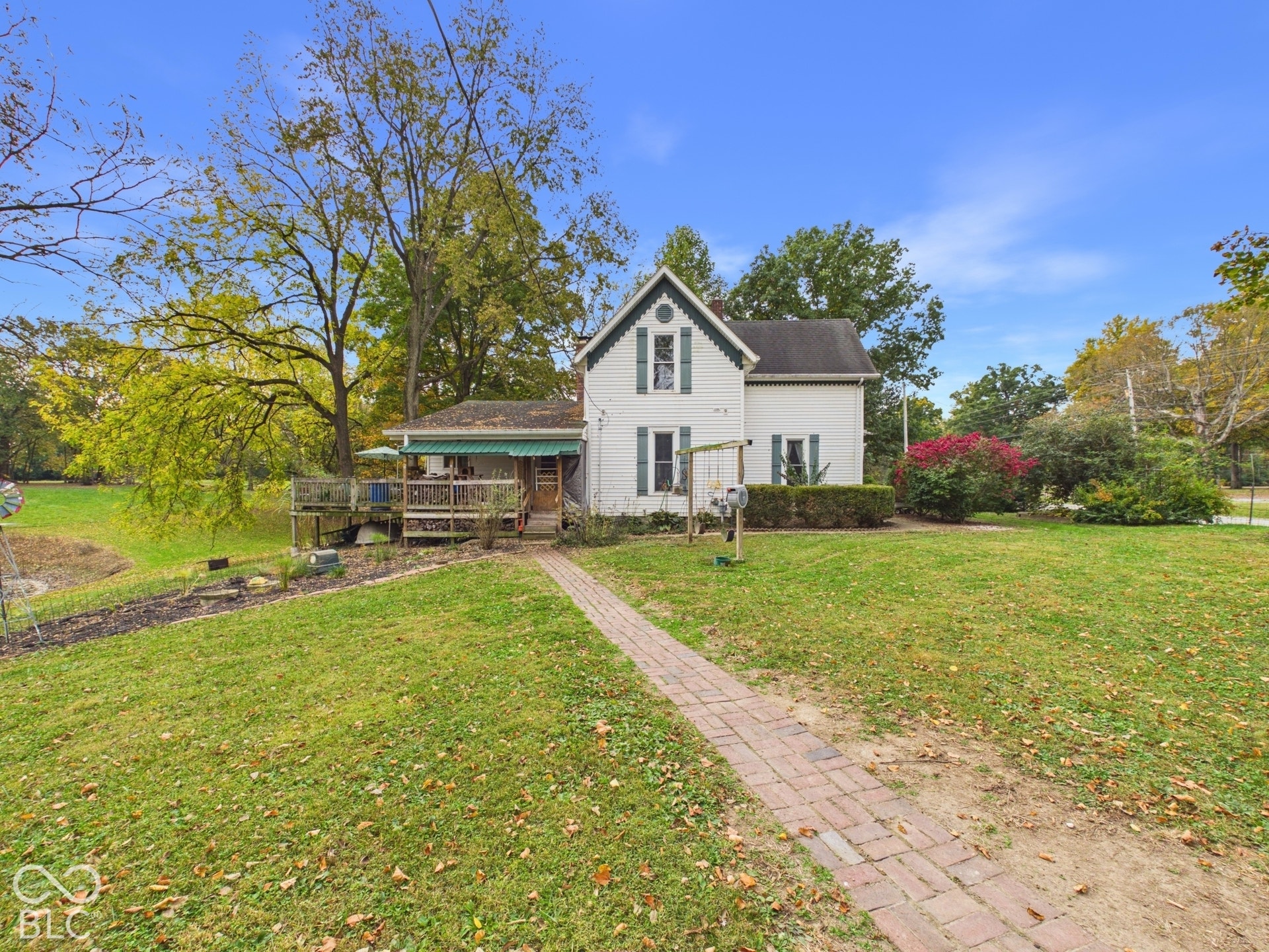 Two-story residence featuring white siding, a steeply pitched roofline with decorative gable trim, a brick paver walkway, and a raised wooden deck with an attached awning
