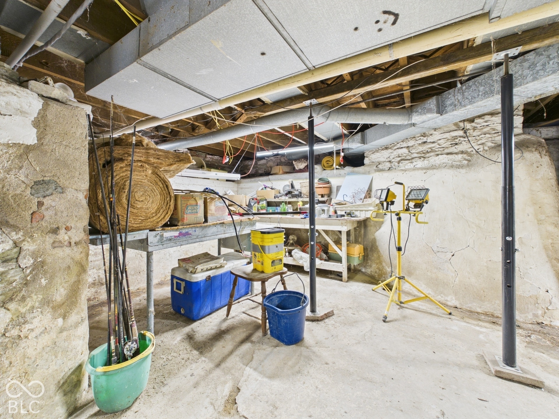 Unfinished basement area featuring exposed stone foundation walls, concrete flooring, and adjustable steel support columns