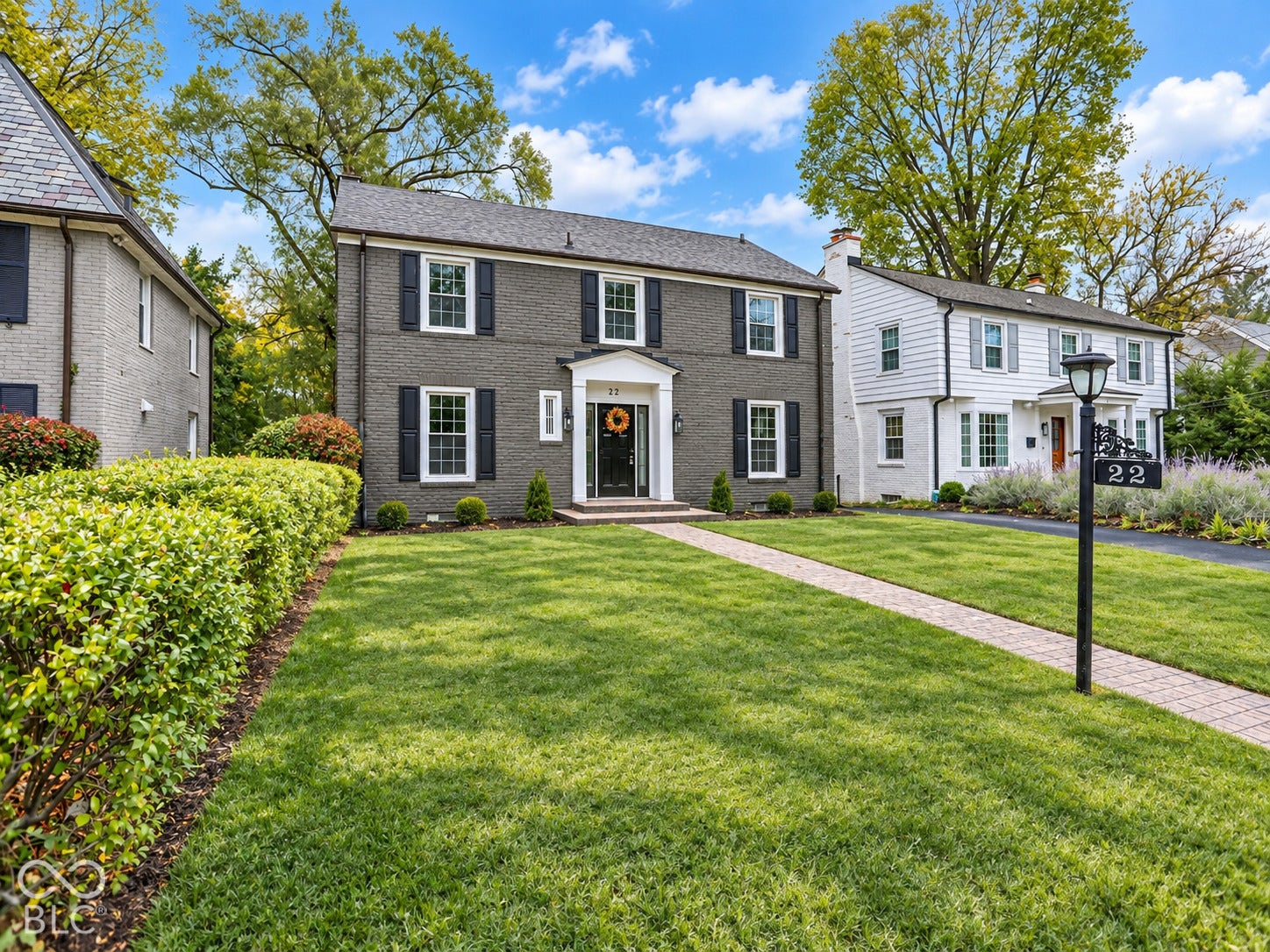 Two-story brick exterior featuring dark-toned masonry, symmetrical window placement, contrasting shutters, a central portico, and a stone-paver walkway