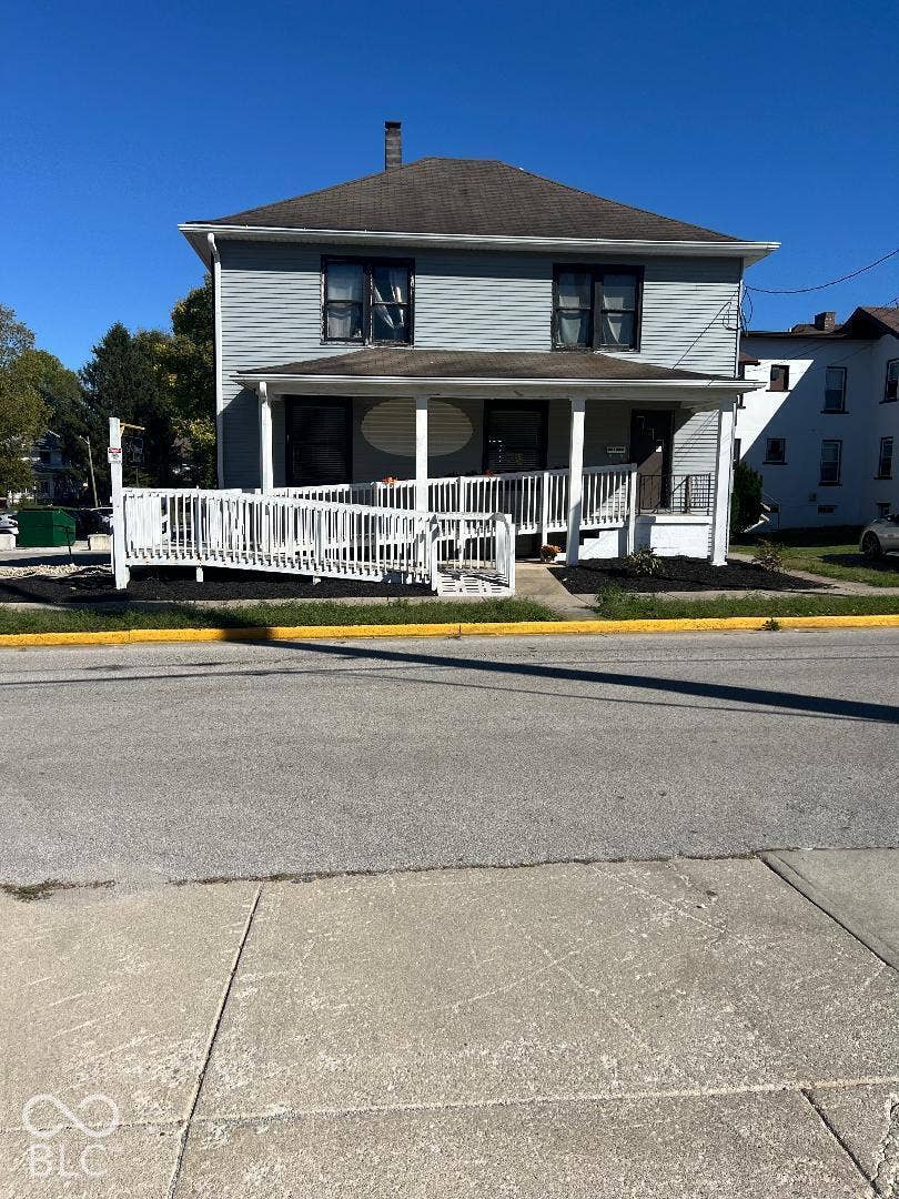 Two-story exterior featuring light-toned horizontal siding, a hipped roof, a covered front porch with white structural columns, and an integrated white ramp railing system